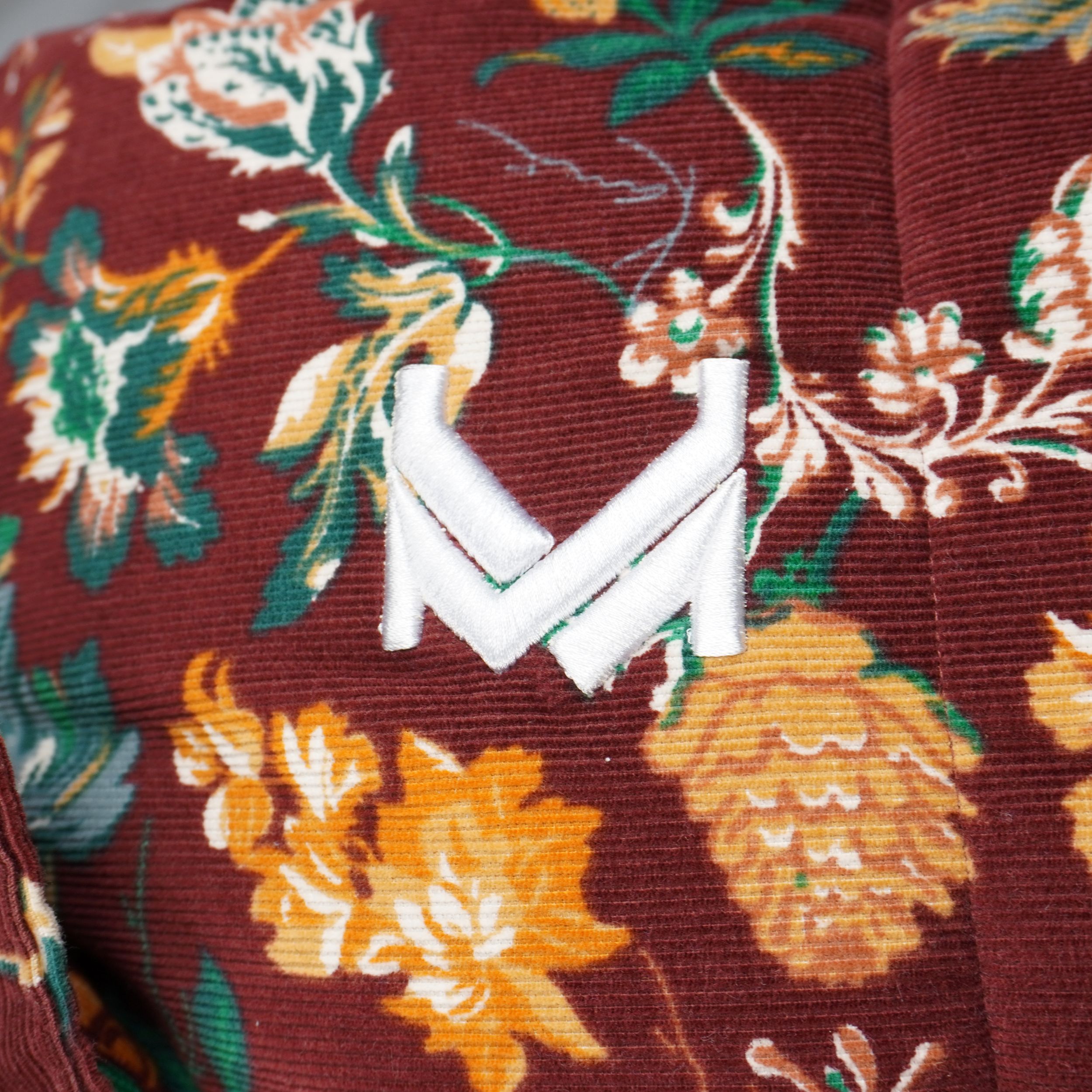Primo piano ravvicinato del monogramma K di Karl Kani ricamato in rilievo con filo bianco sul petto del gilet in velluto.