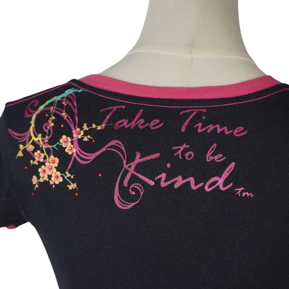 Primo piano del motto Take Time to be Kind stampato in corsivo fucsia sul retro del collo della maglietta