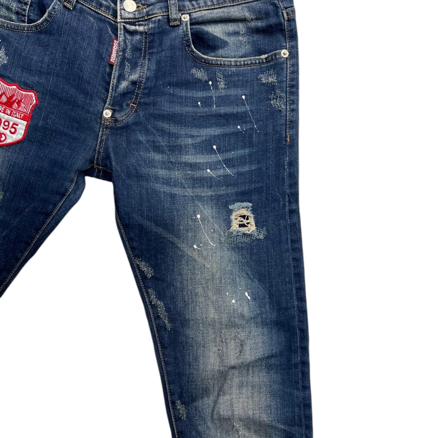 Primo piano dei patch stile college e scout ricamati sulla coscia destra dei jeans.