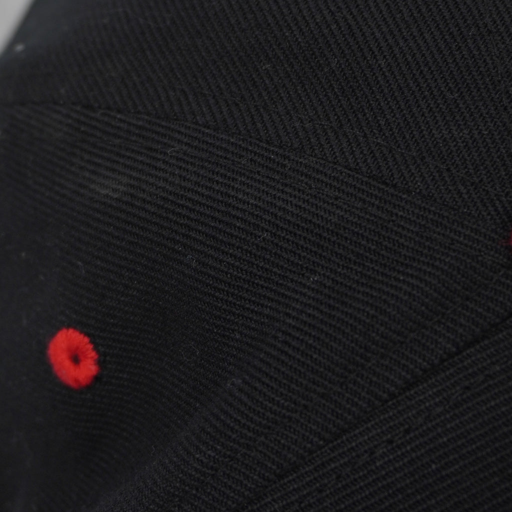 Particolare degli occhielli di ventilazione ricamati in rosso a contrasto sulla corona nera del cappellino.