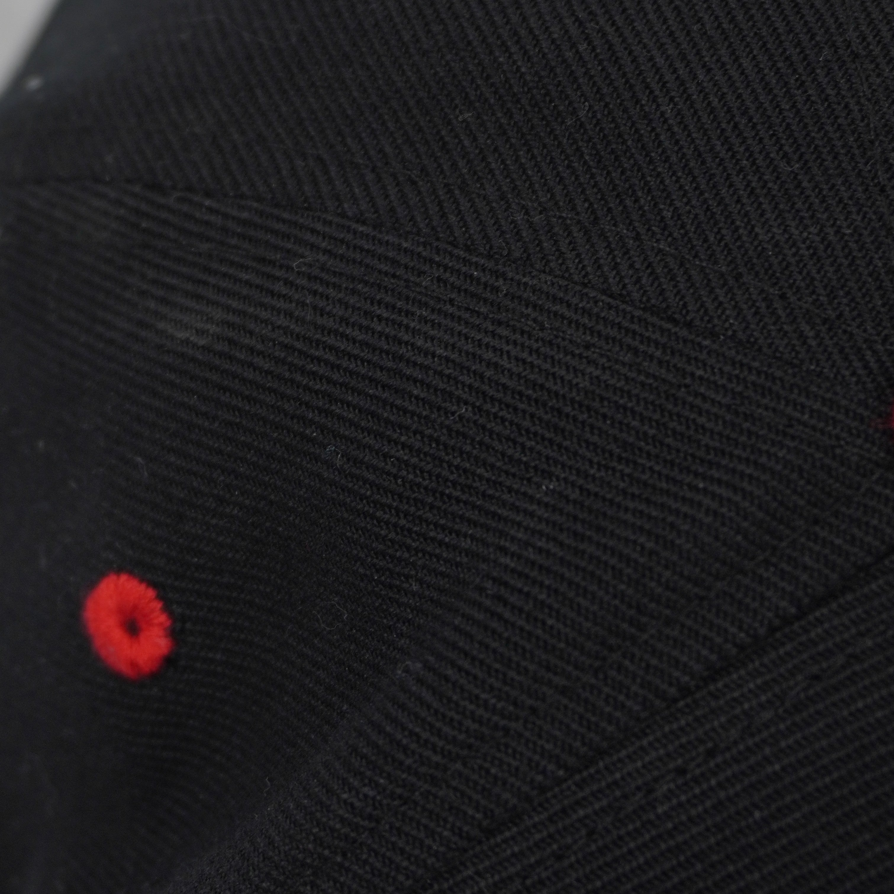 Particolare degli occhielli di ventilazione ricamati in rosso a contrasto sulla corona nera del cappellino.