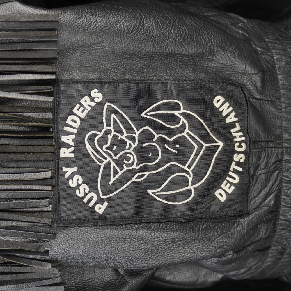 Primo piano della patch in tessuto nero sul retro della giacca con grafica pin-up bianca e scritte.