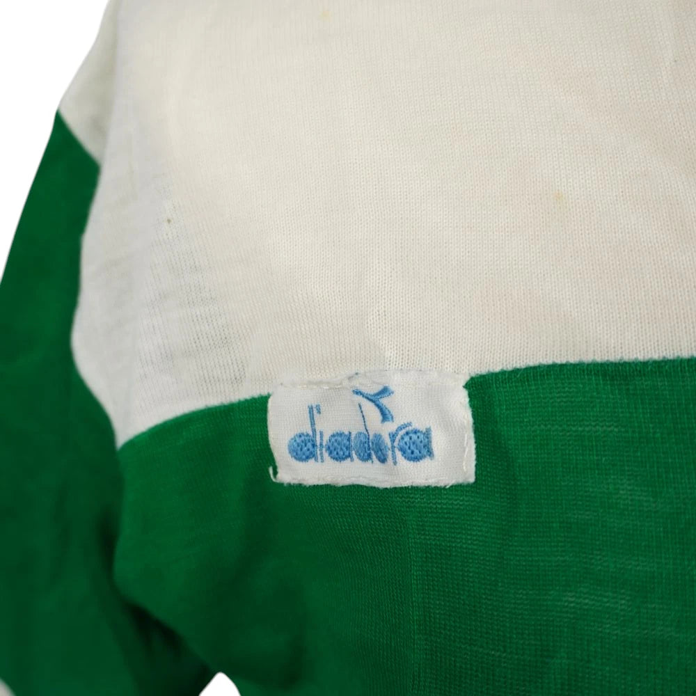 Dettaglio della patch con logo Diadora azzurro cucito sul petto tra il tessuto bianco e verde