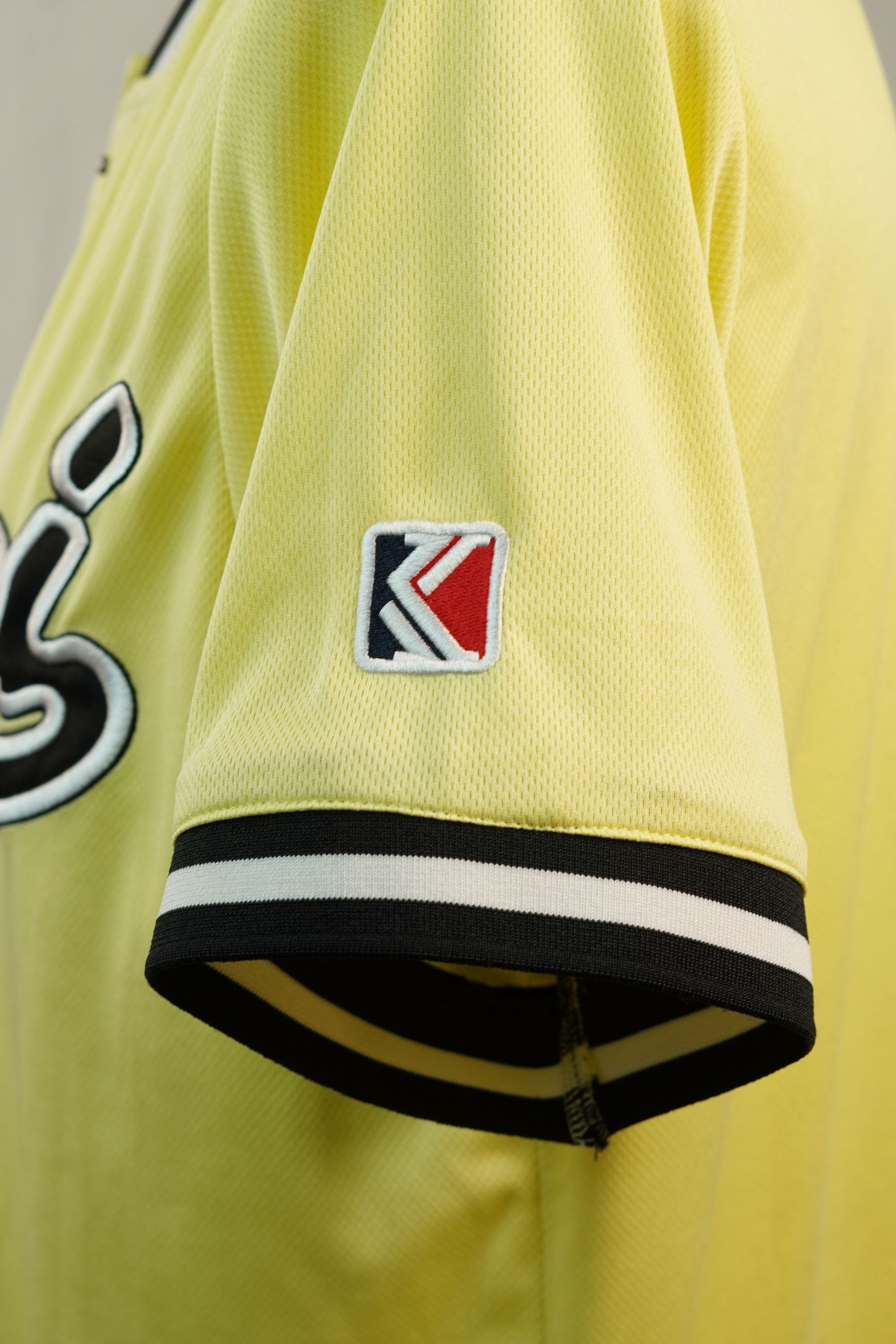 Inquadratura ravvicinata della manica corta che mostra una piccola patch quadrata ricamata con i colori iconici del brand Karl Kani.