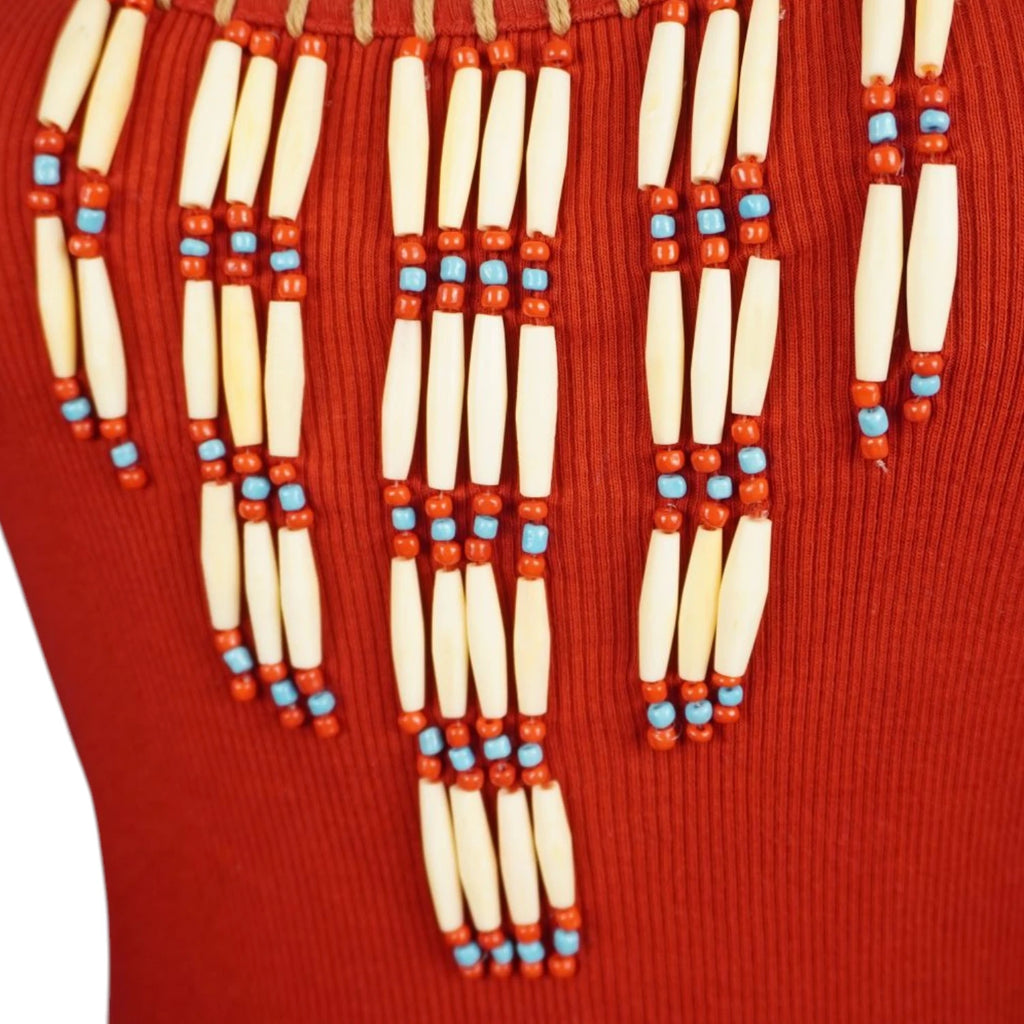 Primo piano del ricamo etnico sul décolleté della canotta con file verticali di perline cilindriche bianche, azzurre e rosse a cascata.