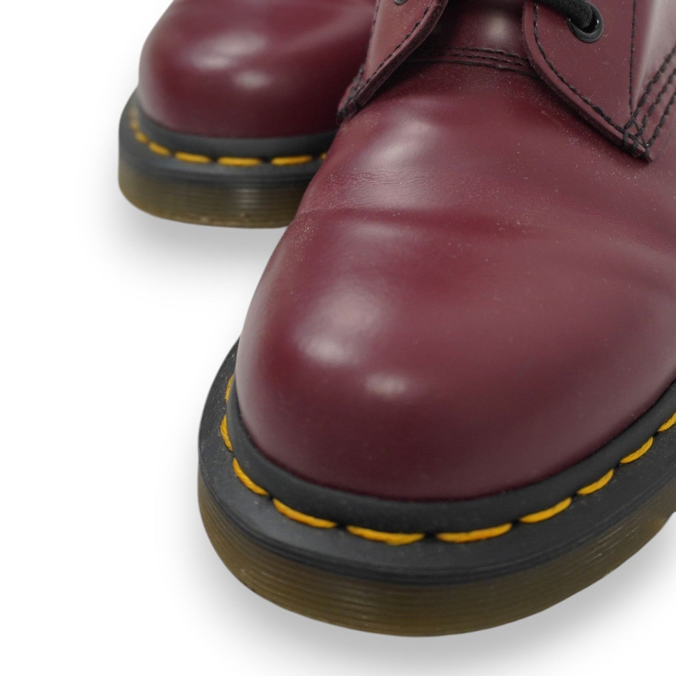 Inquadratura ravvicinata sulla punta arrotondata in pelle bordeaux e sulle iconiche cuciture gialle a contrasto sulla suola Dr. Martens.