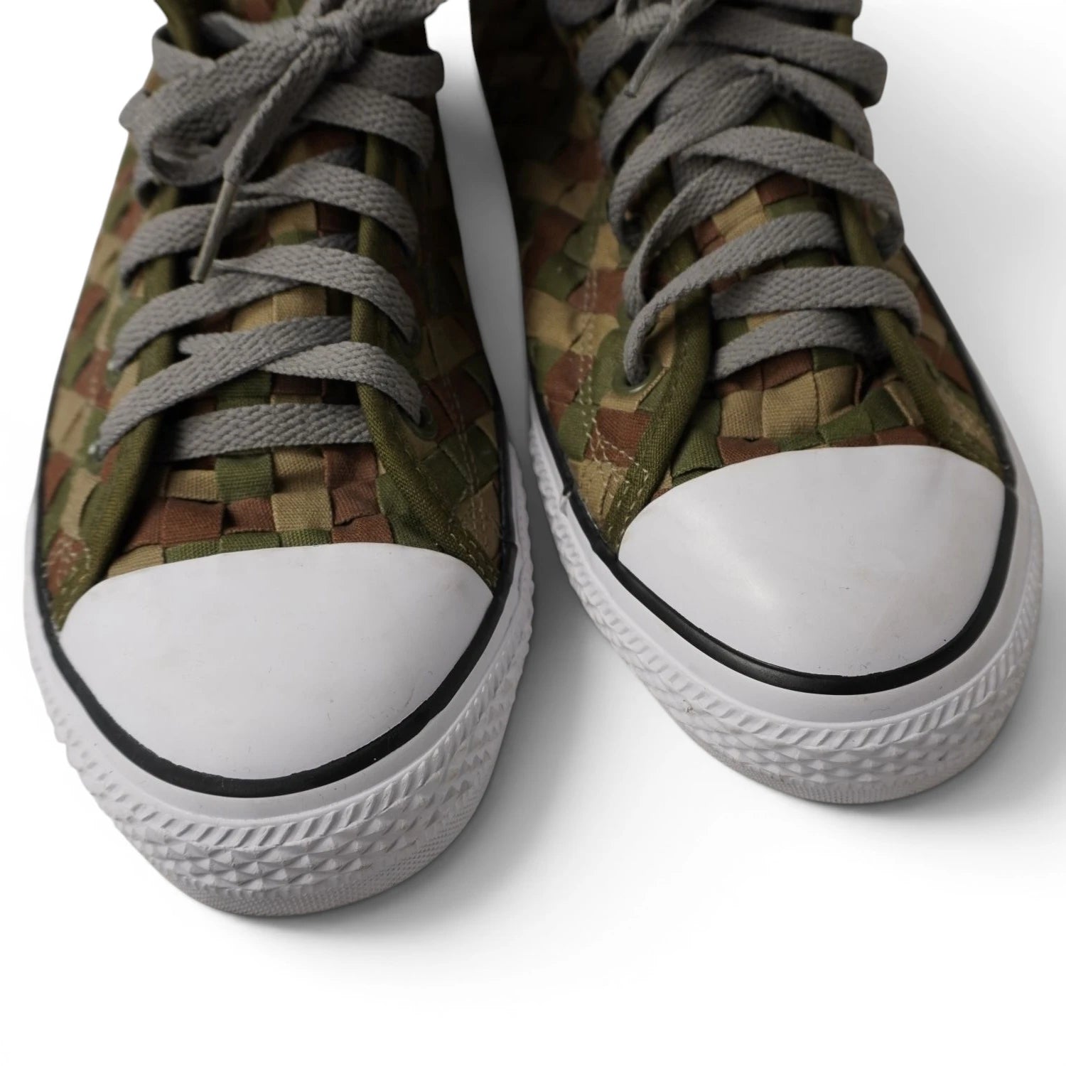 Primo piano ravvicinato dei puntali in gomma bianca e dei lacci grigi delle Converse intrecciate mimetiche.