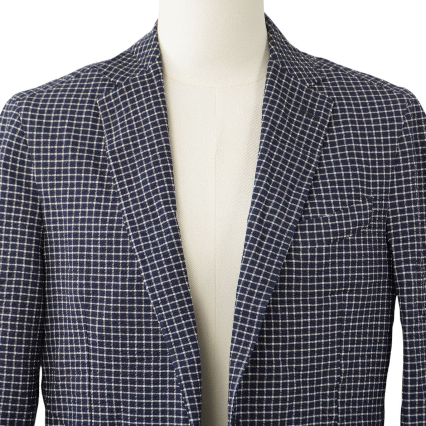 Primo piano frontale del colletto e dei revers a lancia della giacca sartoriale a quadretti blu navy e bianchi.