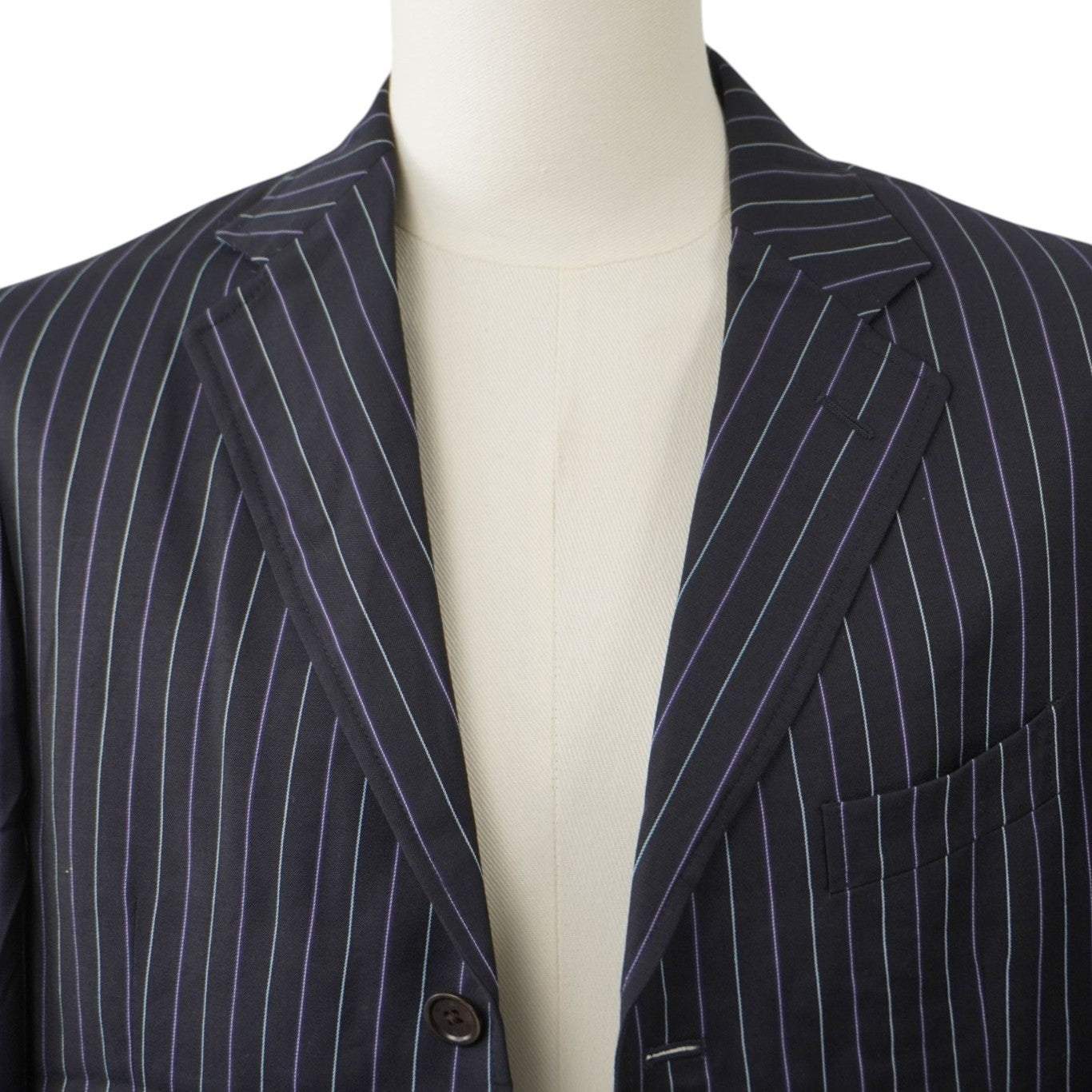 Primo piano frontale dei revers classici e della scollatura a V della giacca sartoriale blu navy a righe sottili bianche.