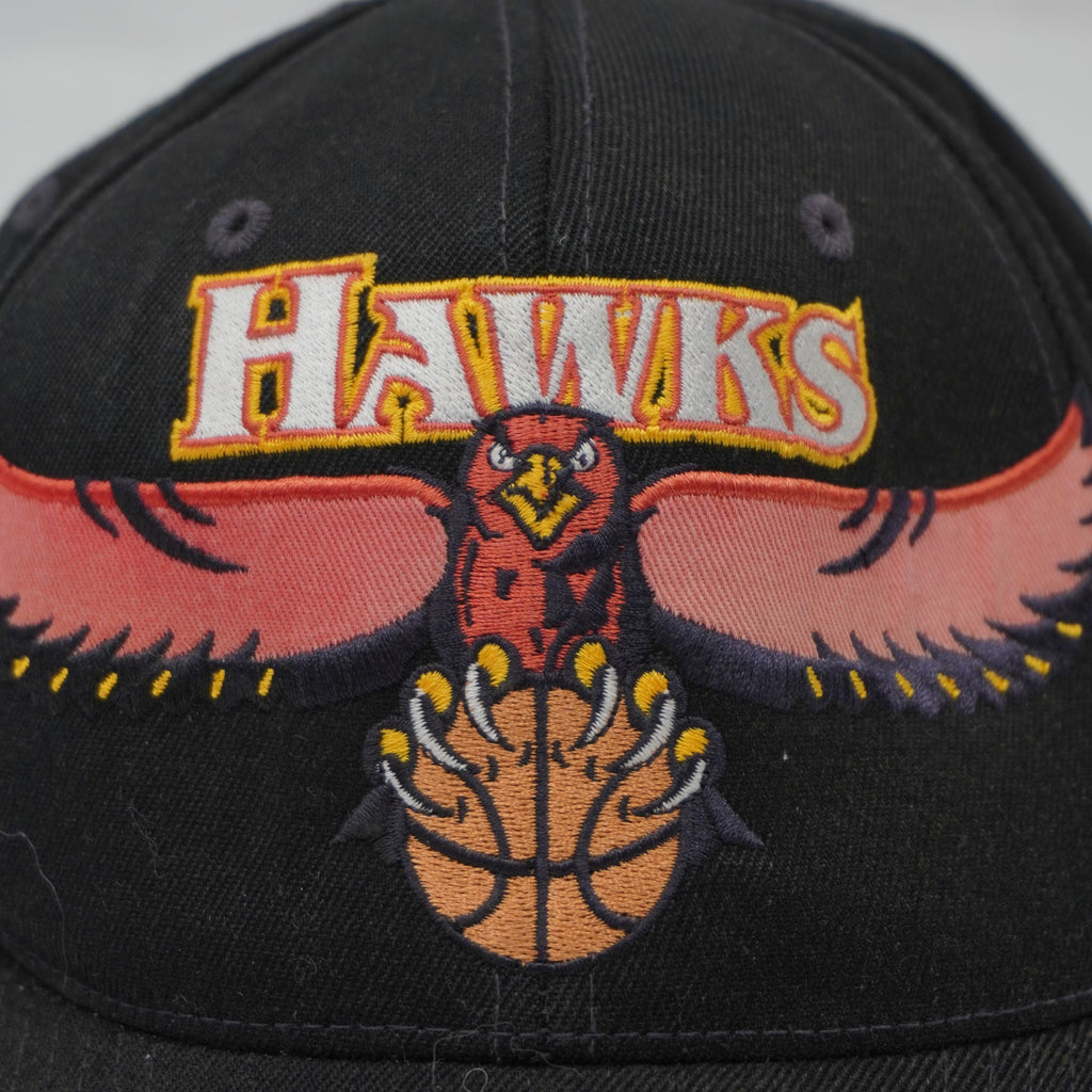 primo piano del ricamo ad alta densità del logo Atlanta Hawks con aquila e palla da basket su corona nera.