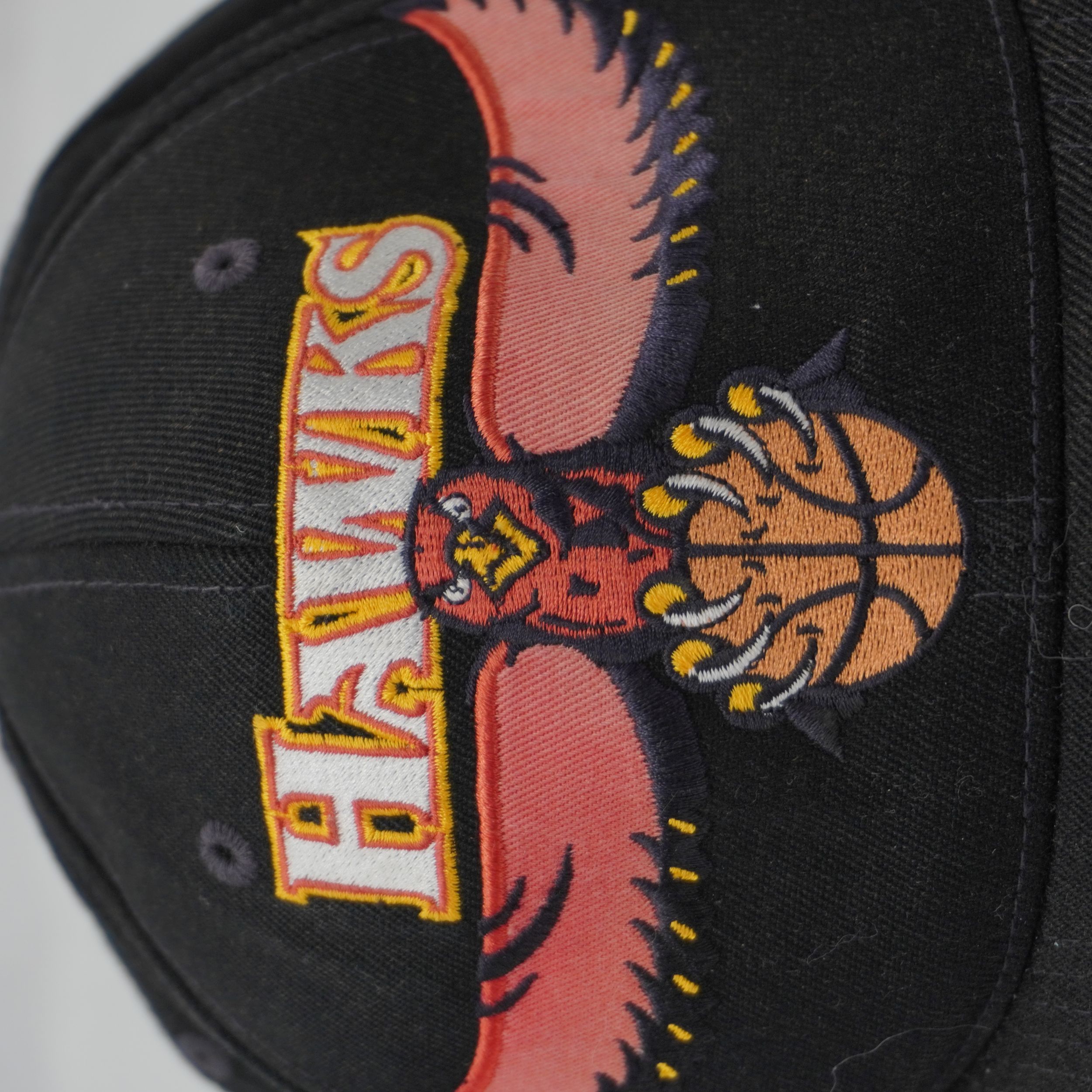 primo piano del ricamo ad alta densità del logo Atlanta Hawks con aquila e palla da basket su corona nera.