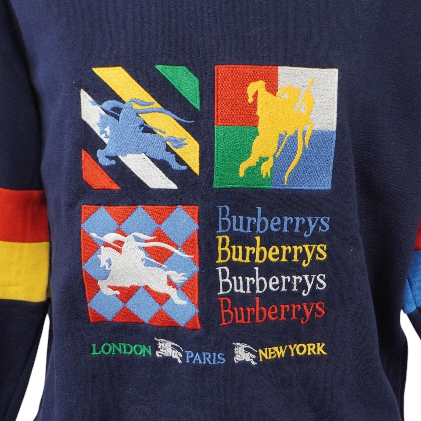 Primo piano frontale del petto con la maxi grafica ricamata a quattro riquadri colorati, l'Equestrian Knight Device e il lettering Burberrys.