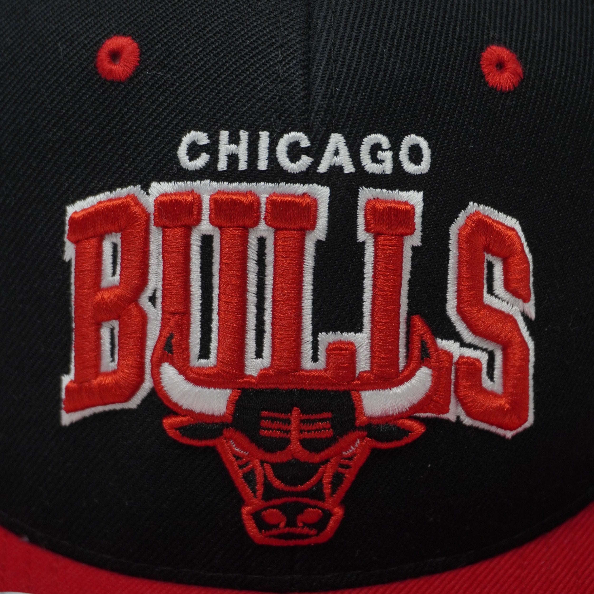 Macro del ricamo frontale ad alta densità "Chicago Bulls" con l'iconico toro rosso, dettaglio di qualità Mitchell & Ness.