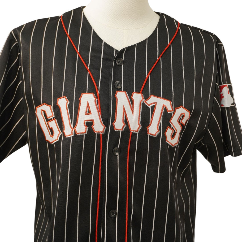 Primo piano del ricamo frontale con la scritta Giants arancione e bianca su tessuto nero pinstripe.