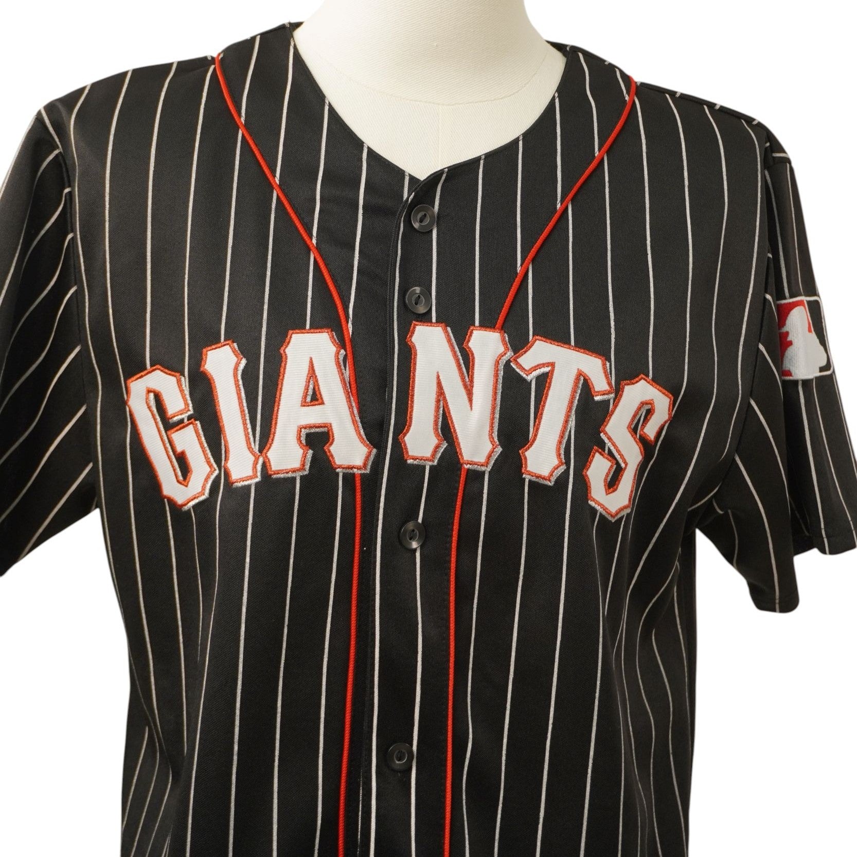 Primo piano del ricamo frontale con la scritta Giants arancione e bianca su tessuto nero pinstripe.