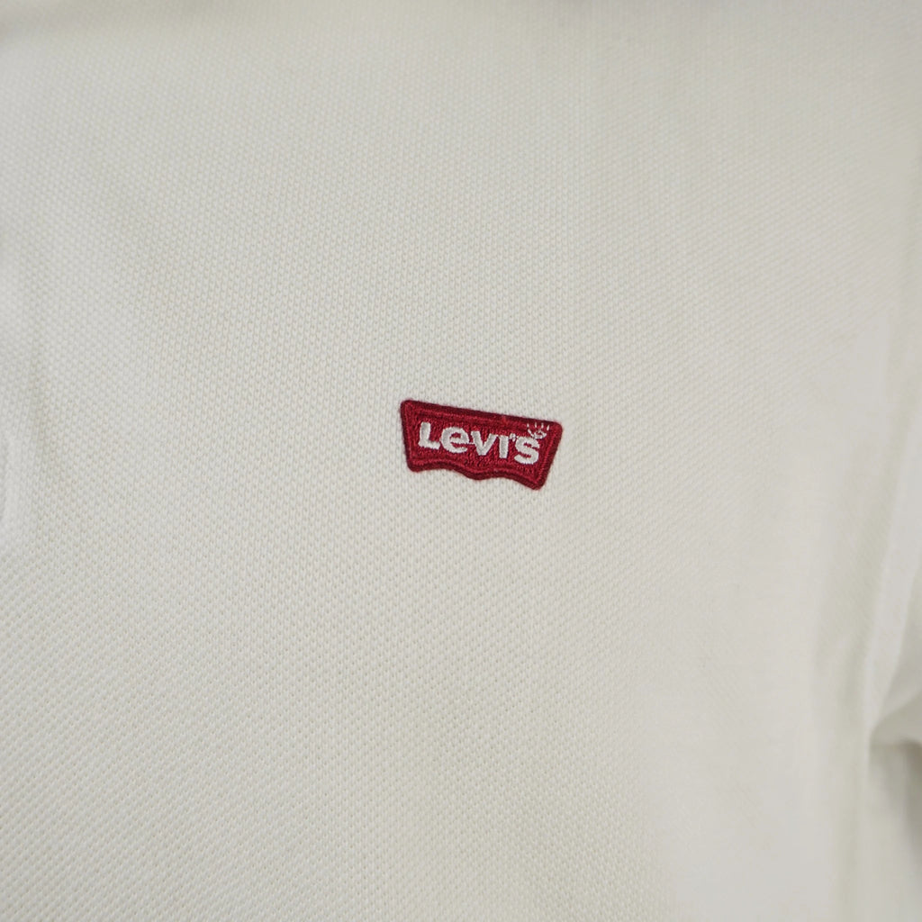 Primo piano del logo Batwing rosso originale di Levi's ricamato finemente sul petto della polo bianca.