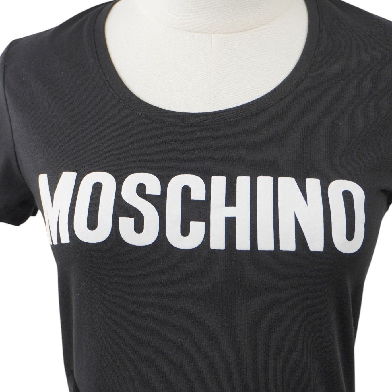  Inquadratura del girocollo della t-shirt nera con la stampa frontale del lettering del brand Moschino in lettere maiuscole bianche.