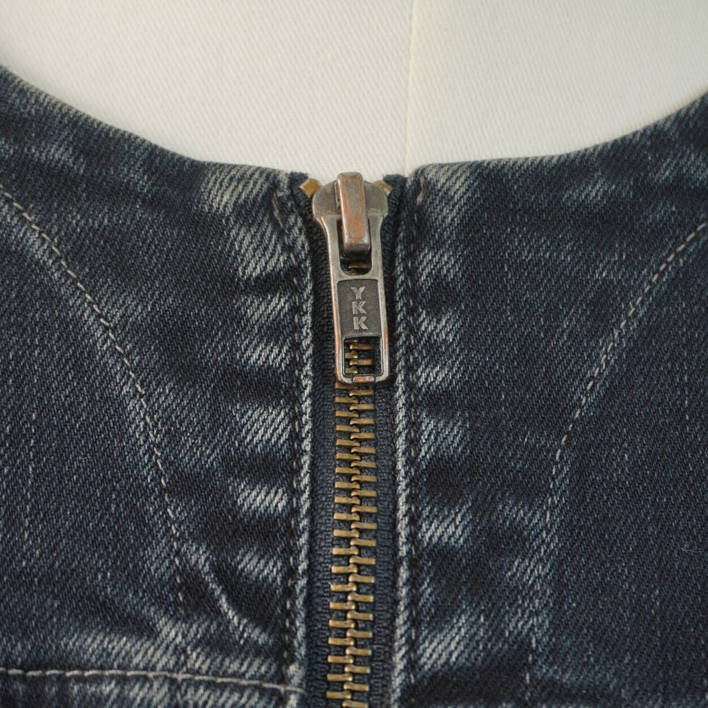 Primo piano dello scollo rotondo senza colletto della giacca, che evidenzia la chiusura lampo in metallo e le impunture sul denim.
