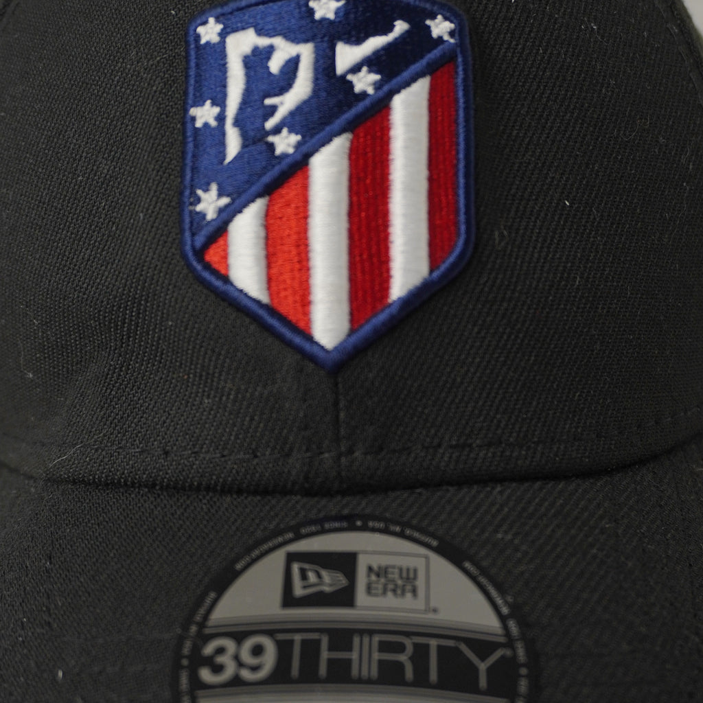 Primo piano del logo ufficiale ricamato ad alta densità dell'Atlético Madrid e dell'adesivo olografico tondo New Era 39THIRTY sulla visiera.