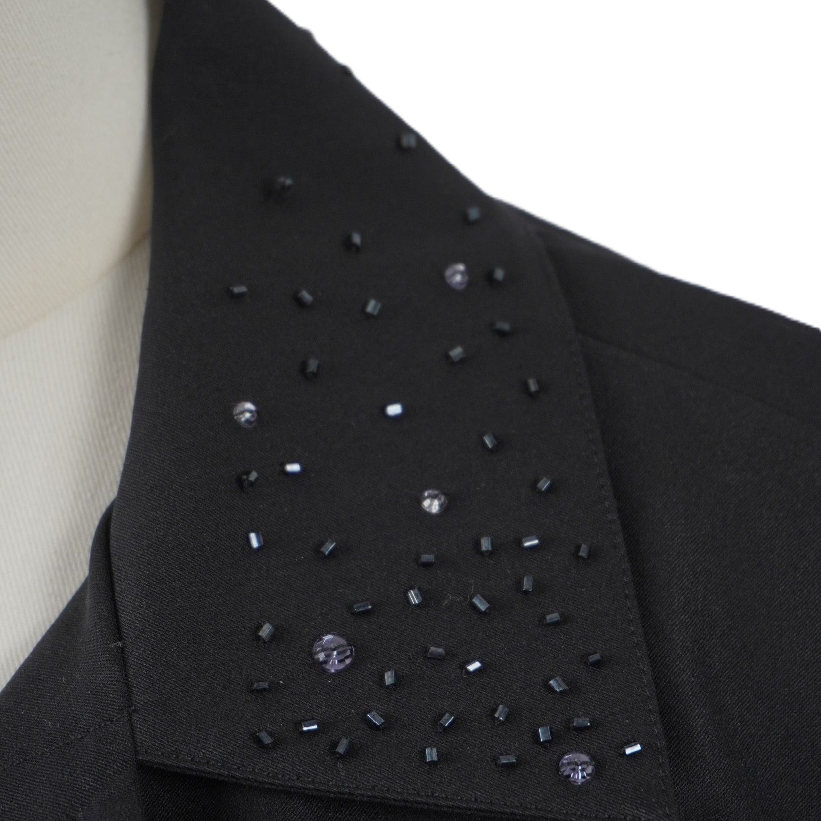 Primo piano ravvicinato delle applicazioni di strass e piccoli brillantini luminosi neri tono su tono sul colletto della giacca.