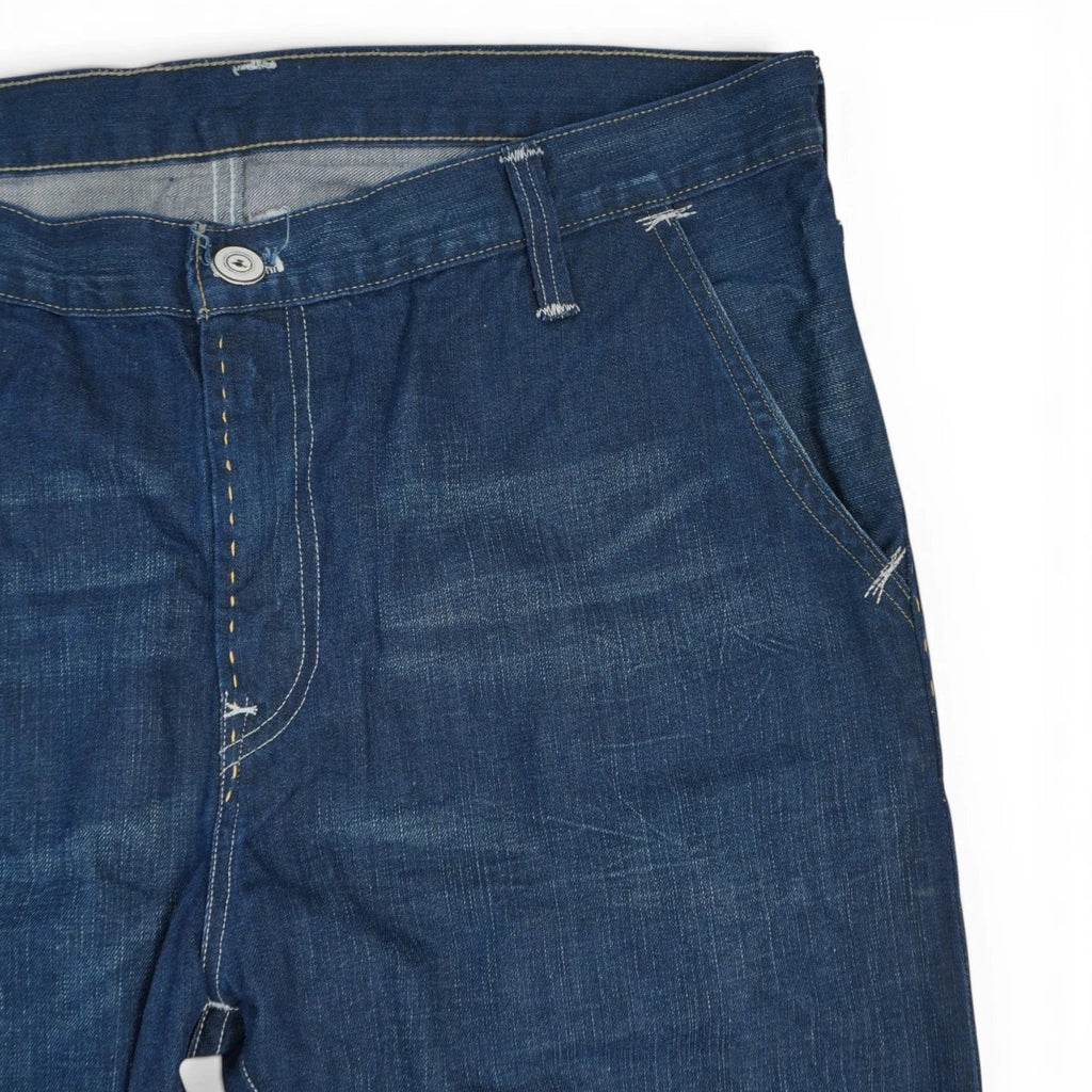Dettaglio ravvicinato della tasca anteriore sinistra stile chino e delle baffature naturali sulla tela denim blu indaco scuro.