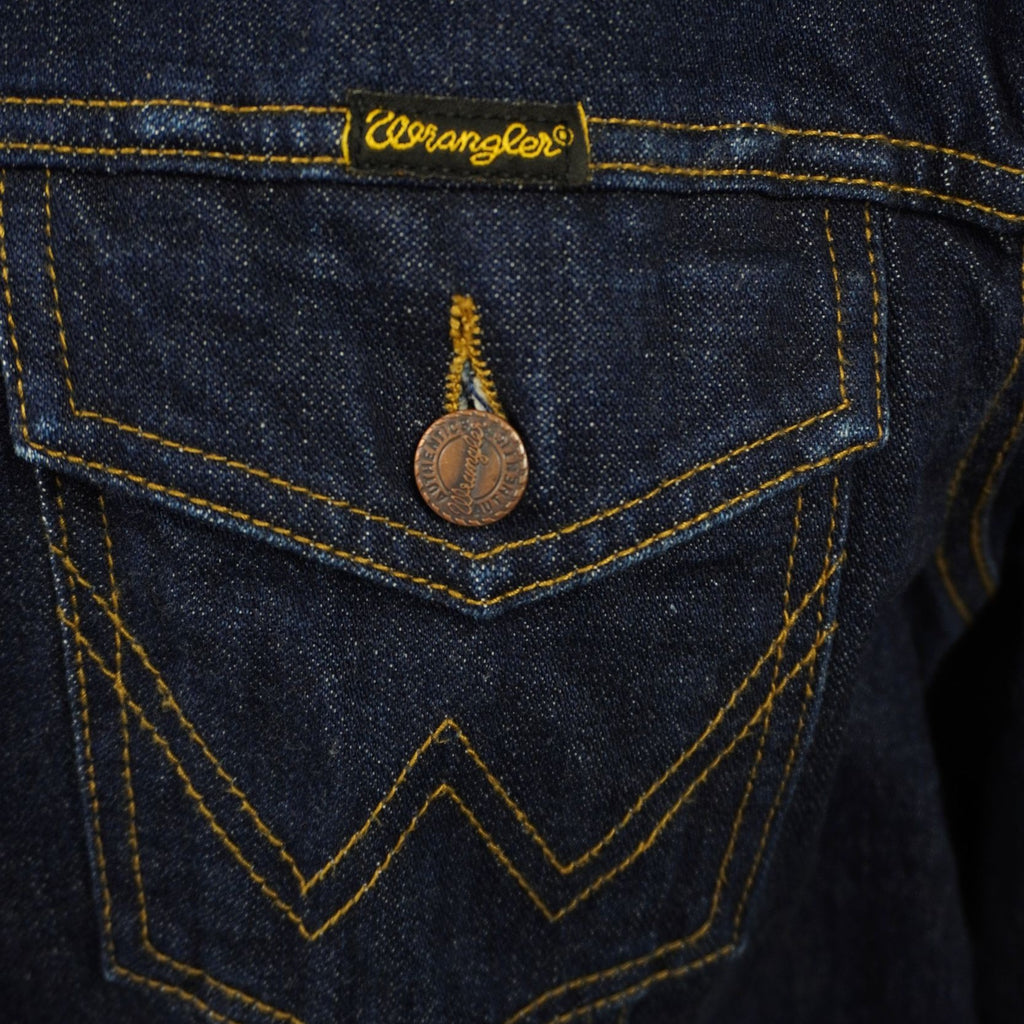 Primo piano della tasca frontale sul petto con patta, bottone metallico e la classica cucitura a forma di "W" simbolo del brand Wrangler.