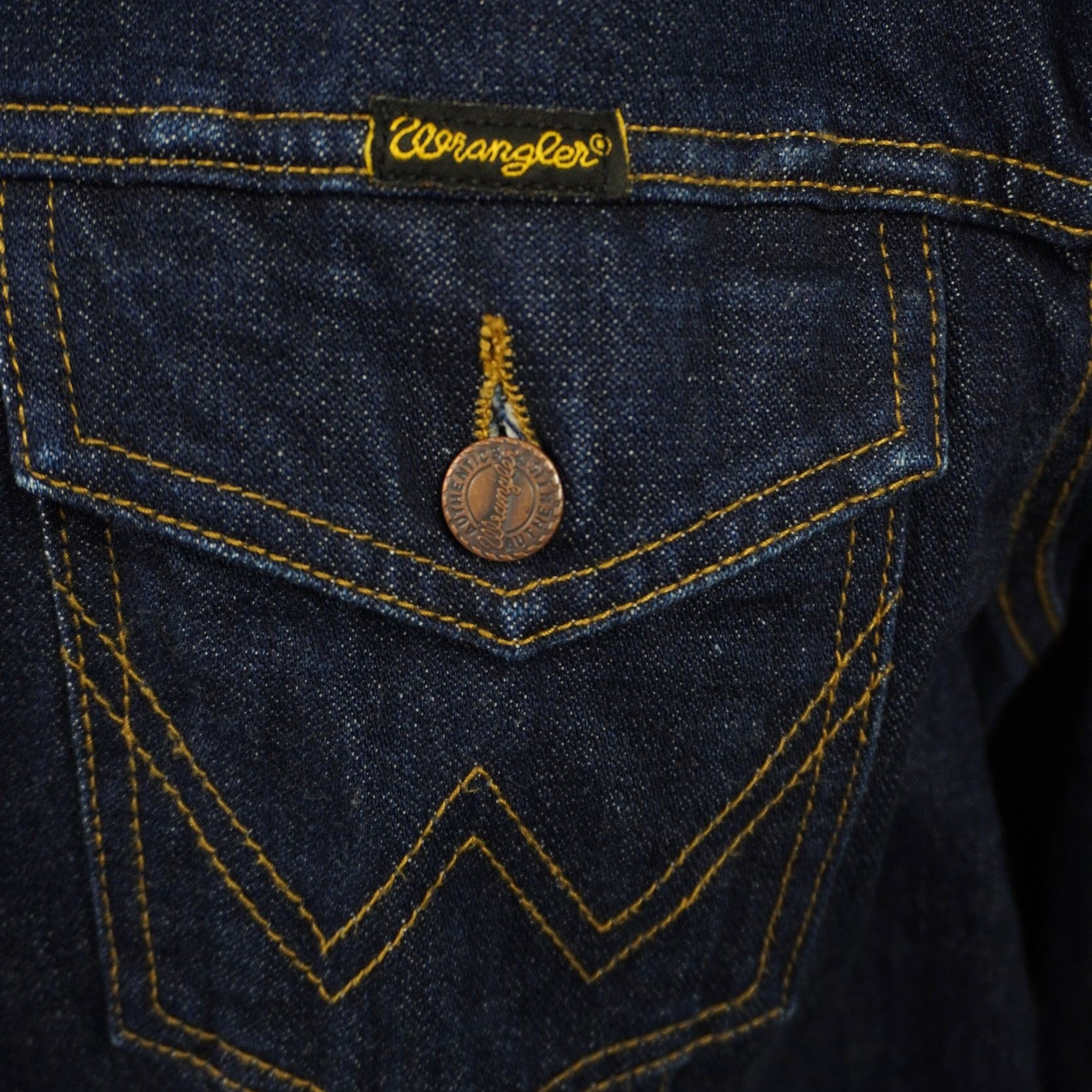 Primo piano della tasca frontale sul petto con patta, bottone metallico e la classica cucitura a forma di "W" simbolo del brand Wrangler.