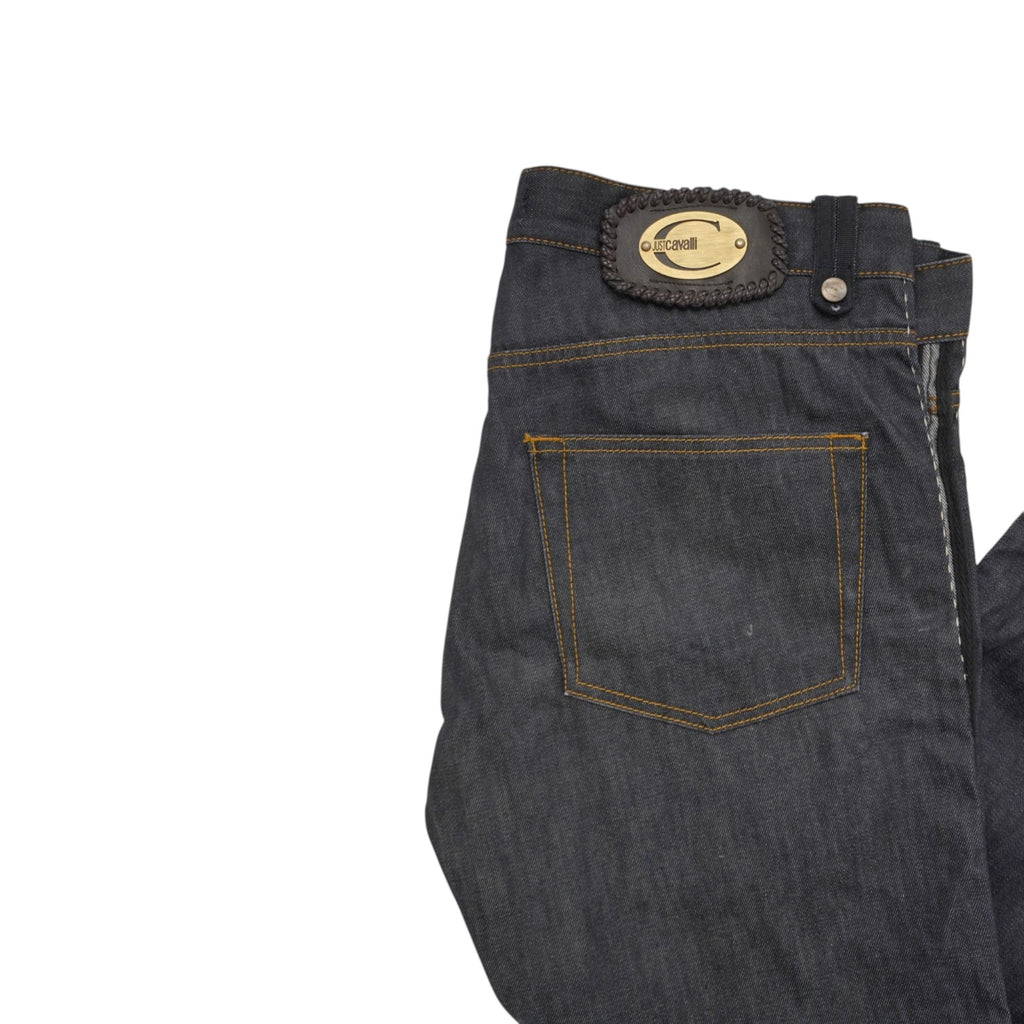  Inquadratura ravvicinata del retro superiore del jeans con la tasca posteriore e la placca metallica dorata ovale cucita sul passante.