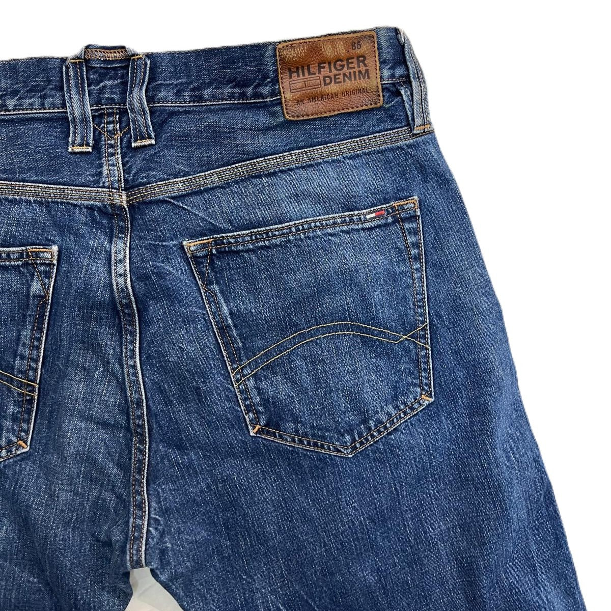 Primo piano della tasca posteriore destra dei jeans Hilfiger Denim con ricamo a onda e salpa in pelle marrone.