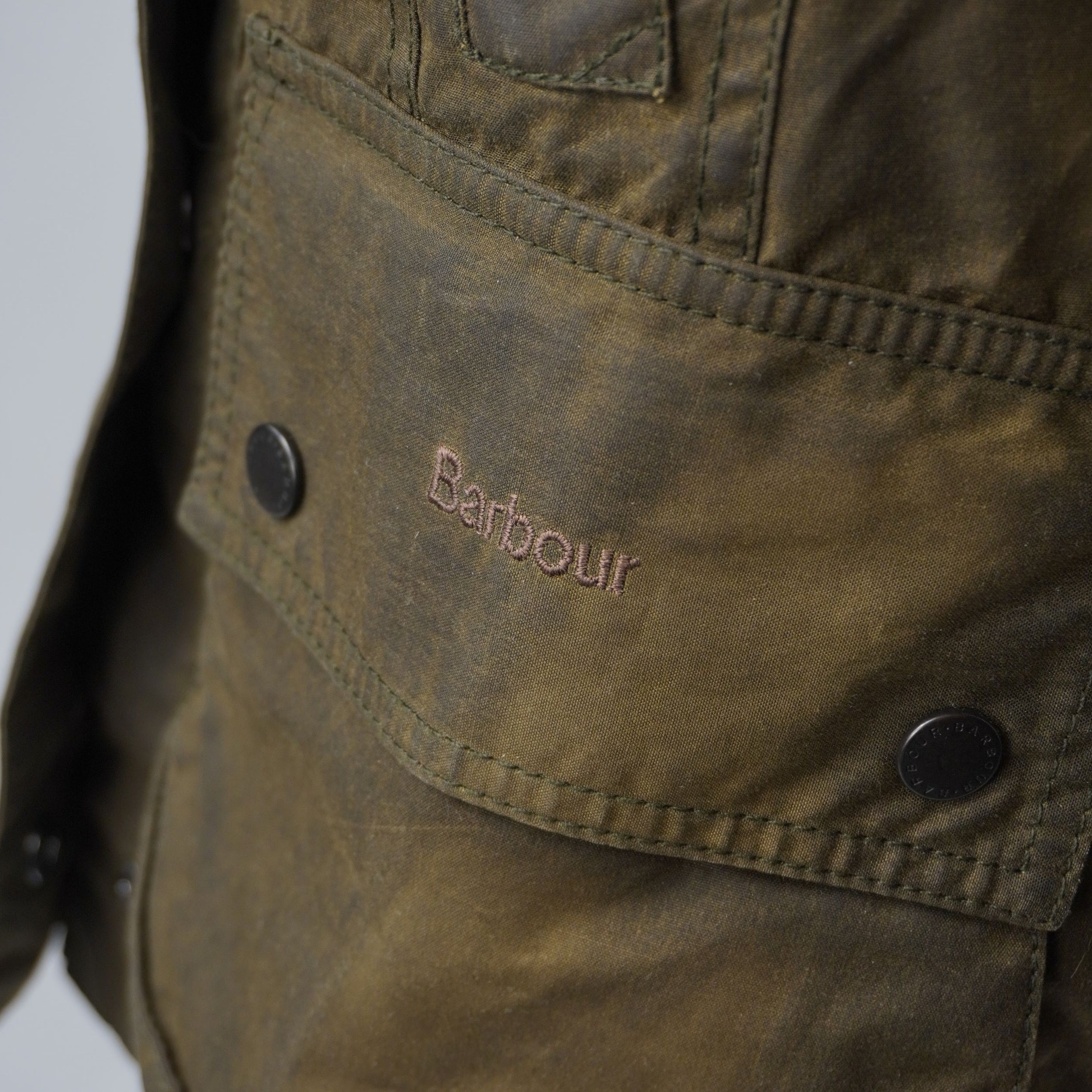 Particolare della tasca frontale a soffietto con il logo Barbour ricamato in filo marrone dorato 
