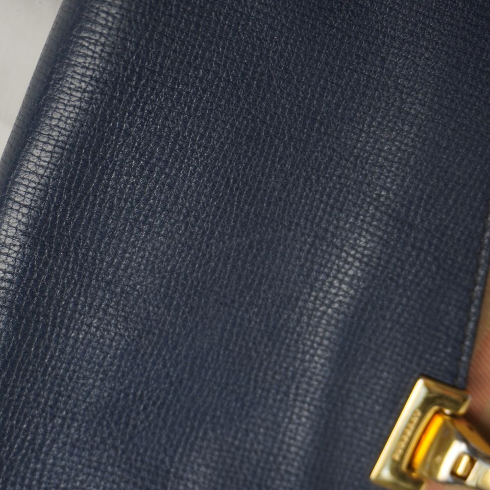 Dettaglio macro della texture della pelle di vitello martellata blu notte sulla patta superiore della borsa.