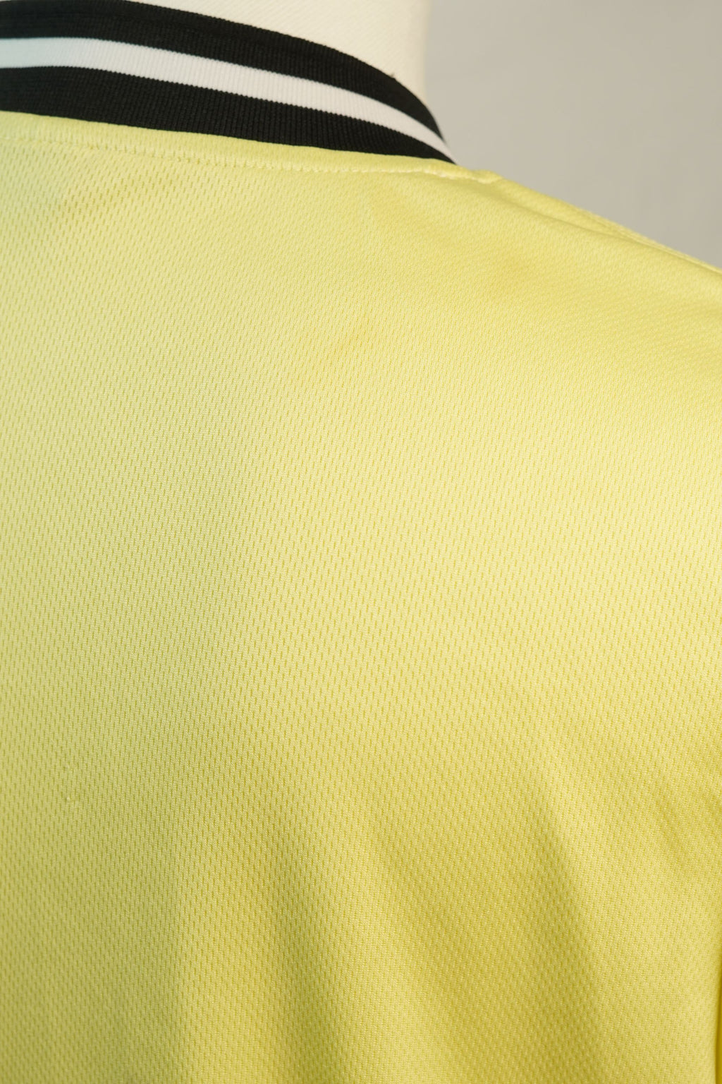Vista ravvicinata della spalla della maglia da baseball, che evidenzia la trama del tessuto tecnico giallo e la finitura della cucitura.
