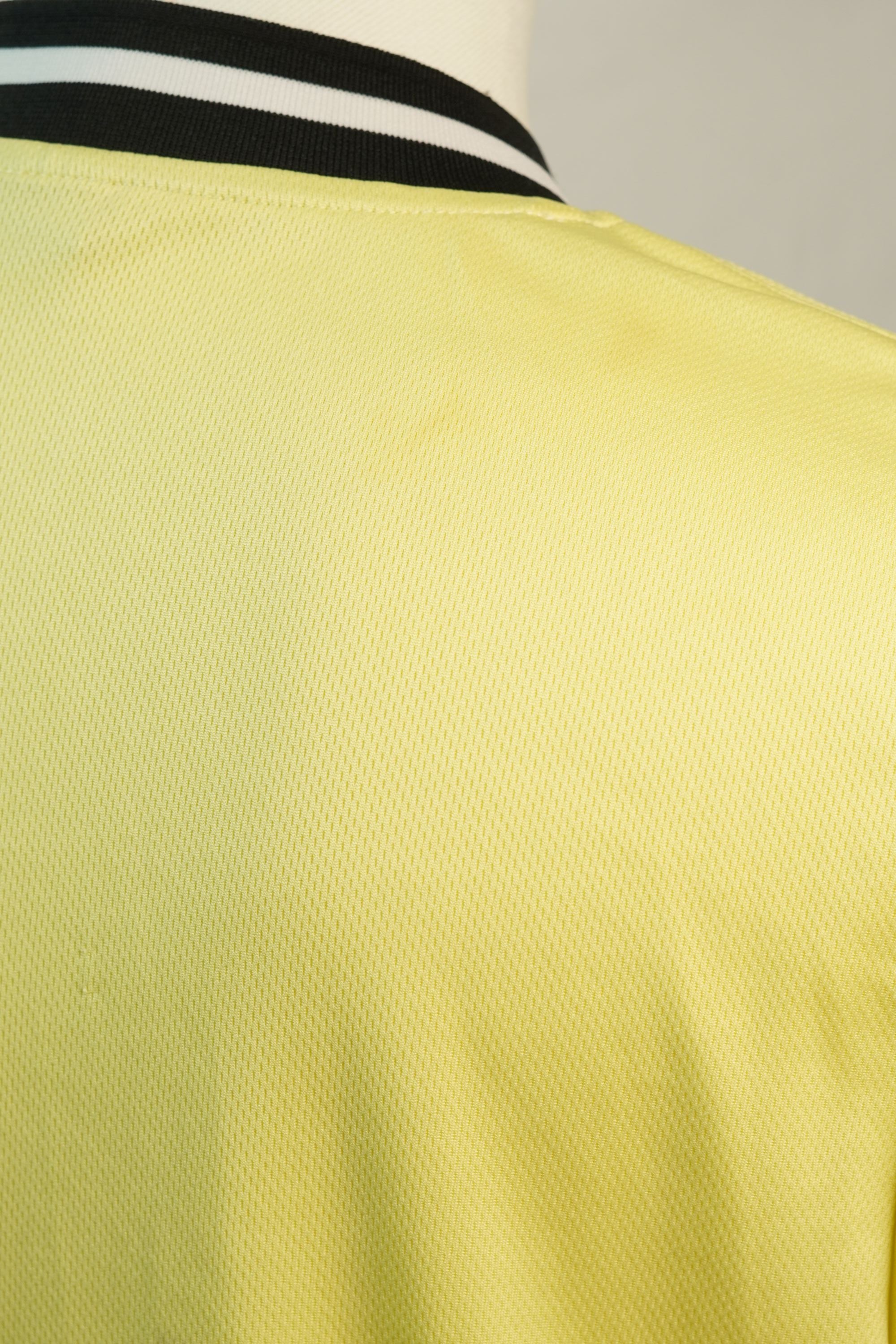 Vista ravvicinata della spalla della maglia da baseball, che evidenzia la trama del tessuto tecnico giallo e la finitura della cucitura.
