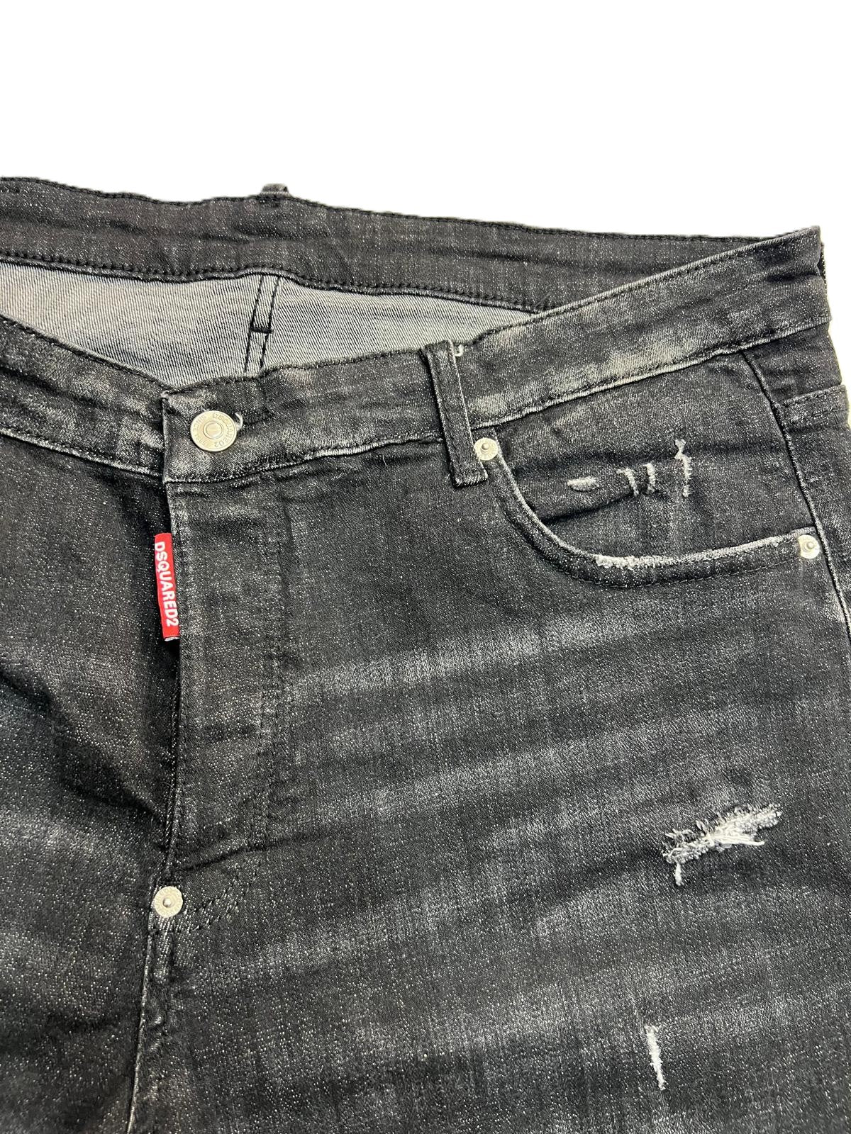 Vista ravvicinata del fascione in vita dei jeans neri con passanti e bottoni metallici a scomparsa.