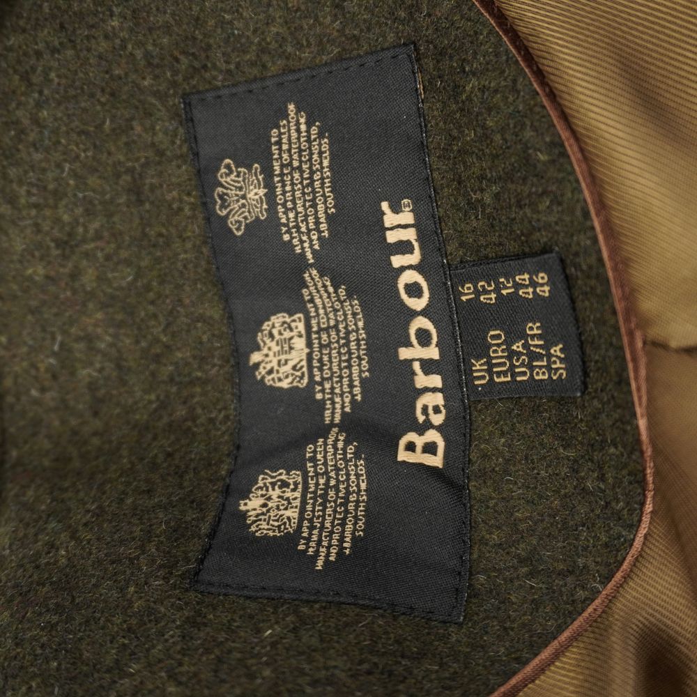 Etichetta interna nera Barbour con i tre stemmi reali dorati e indicazione delle taglie internazionali.
