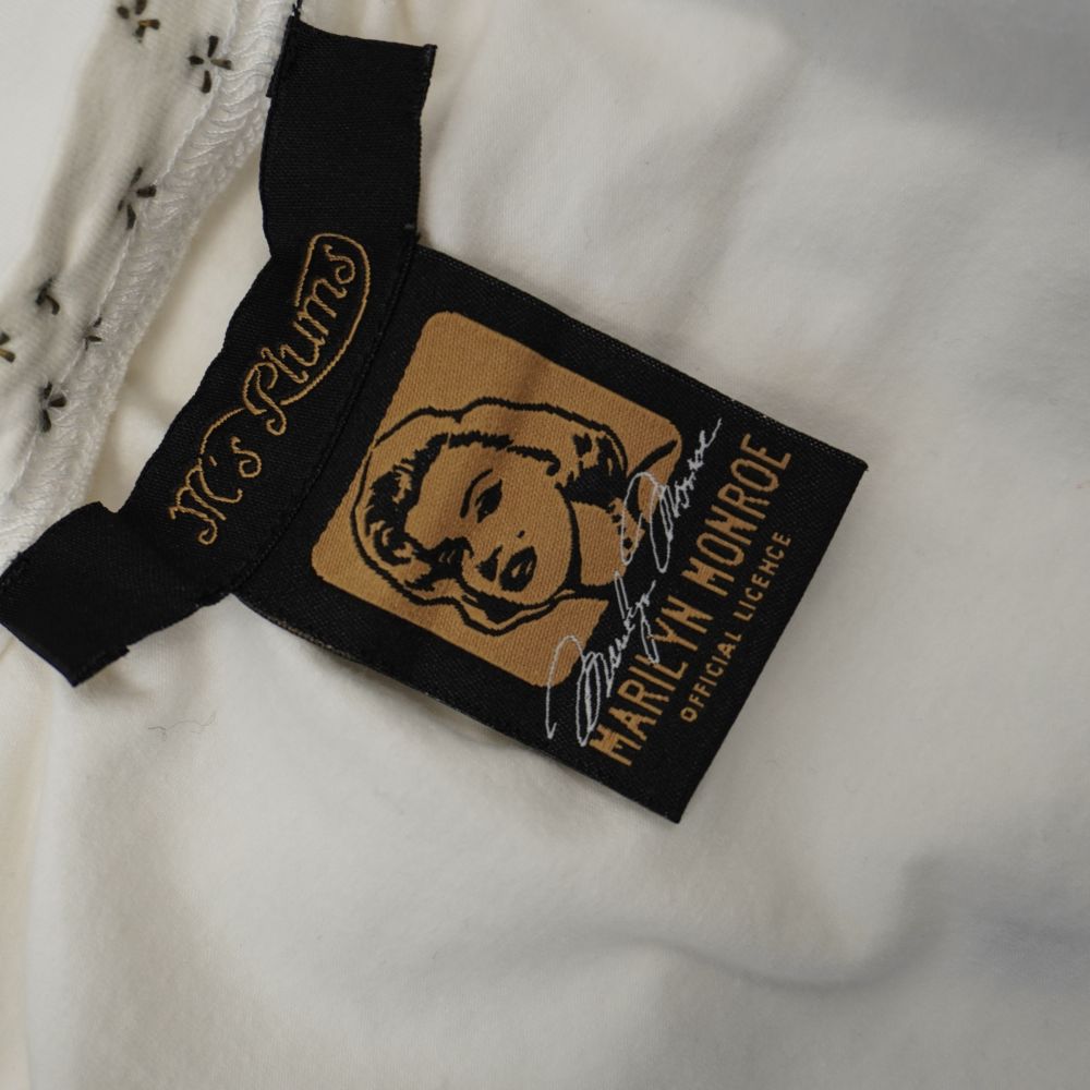 Etichetta interna in tessuto nero del brand M's Plums accanto al cartellino dorato di licenza ufficiale Marilyn Monroe Official Licence.