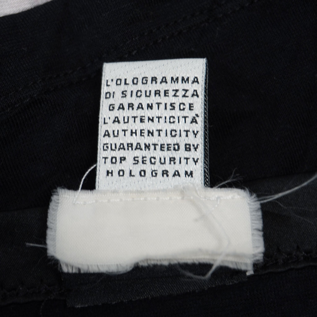 Dettaglio del cartellino interno in tessuto bianco con la dicitura sulla garanzia di autenticità tramite ologramma di sicurezza.