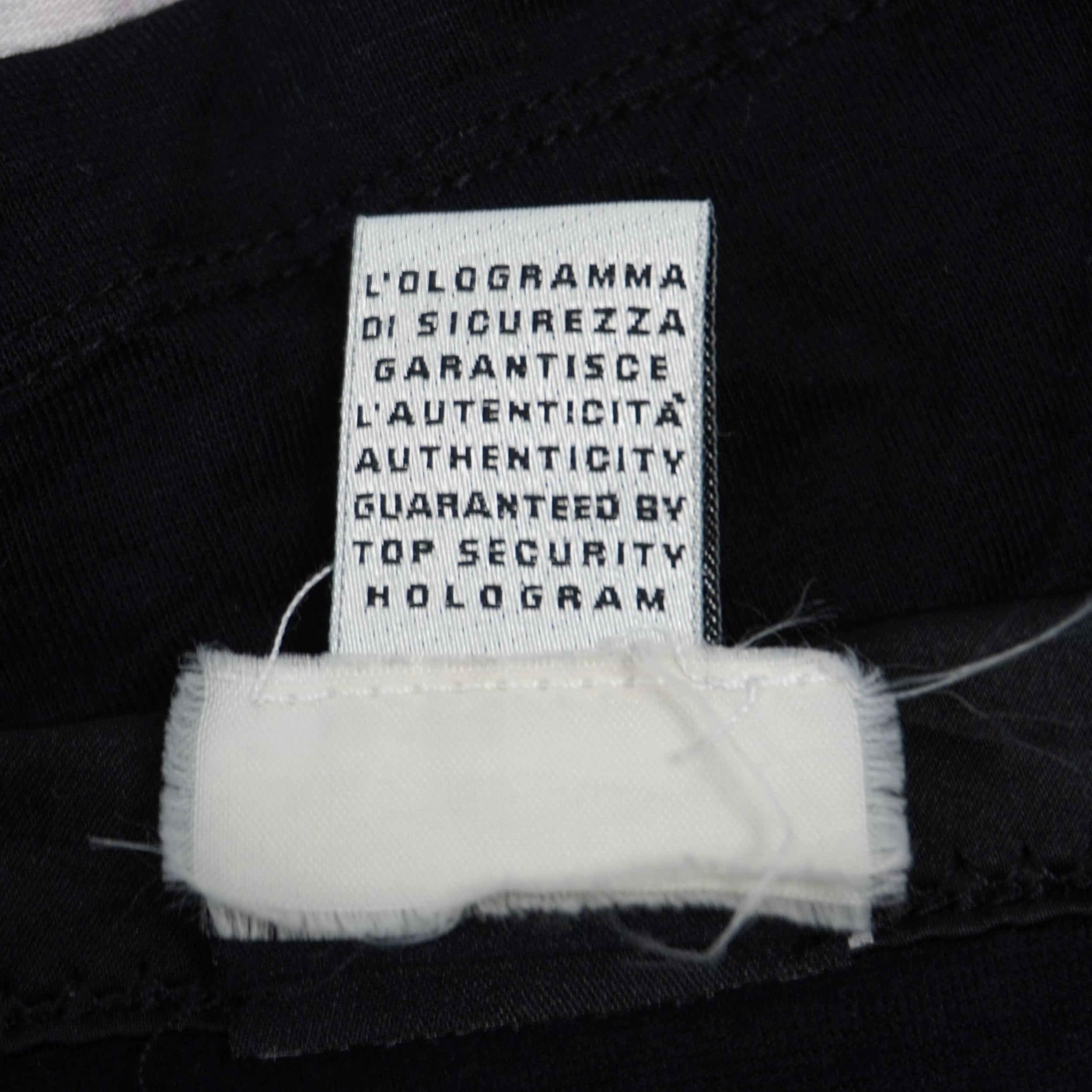 Dettaglio del cartellino interno in tessuto bianco con la dicitura sulla garanzia di autenticità tramite ologramma di sicurezza.