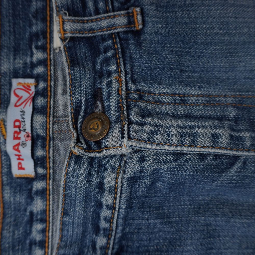 Primo piano del bottone centrale in metallo inciso e dell'etichetta in tessuto jacquard Phard Jeans.