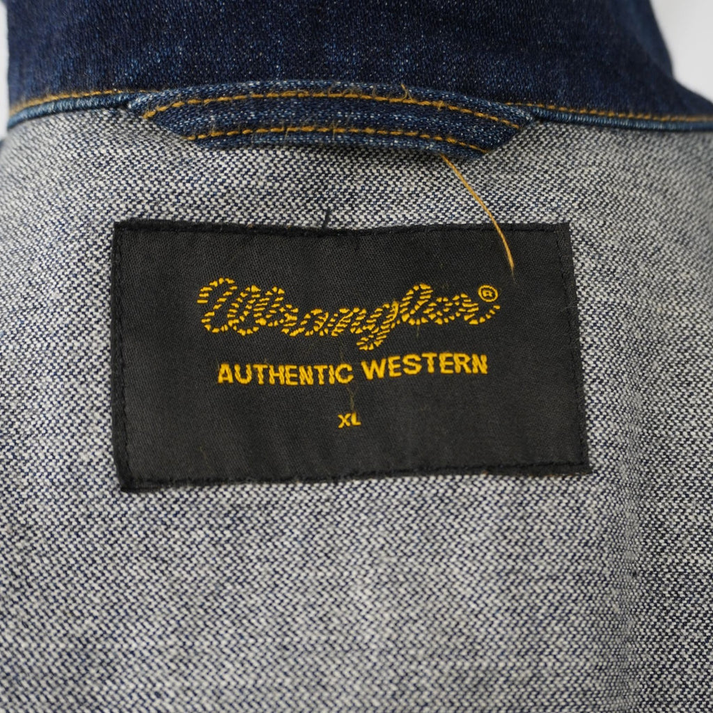 Dettaglio dell'etichetta rettangolare nera con logo Wrangler giallo cucita all'interno del colletto, indicante la taglia XL.