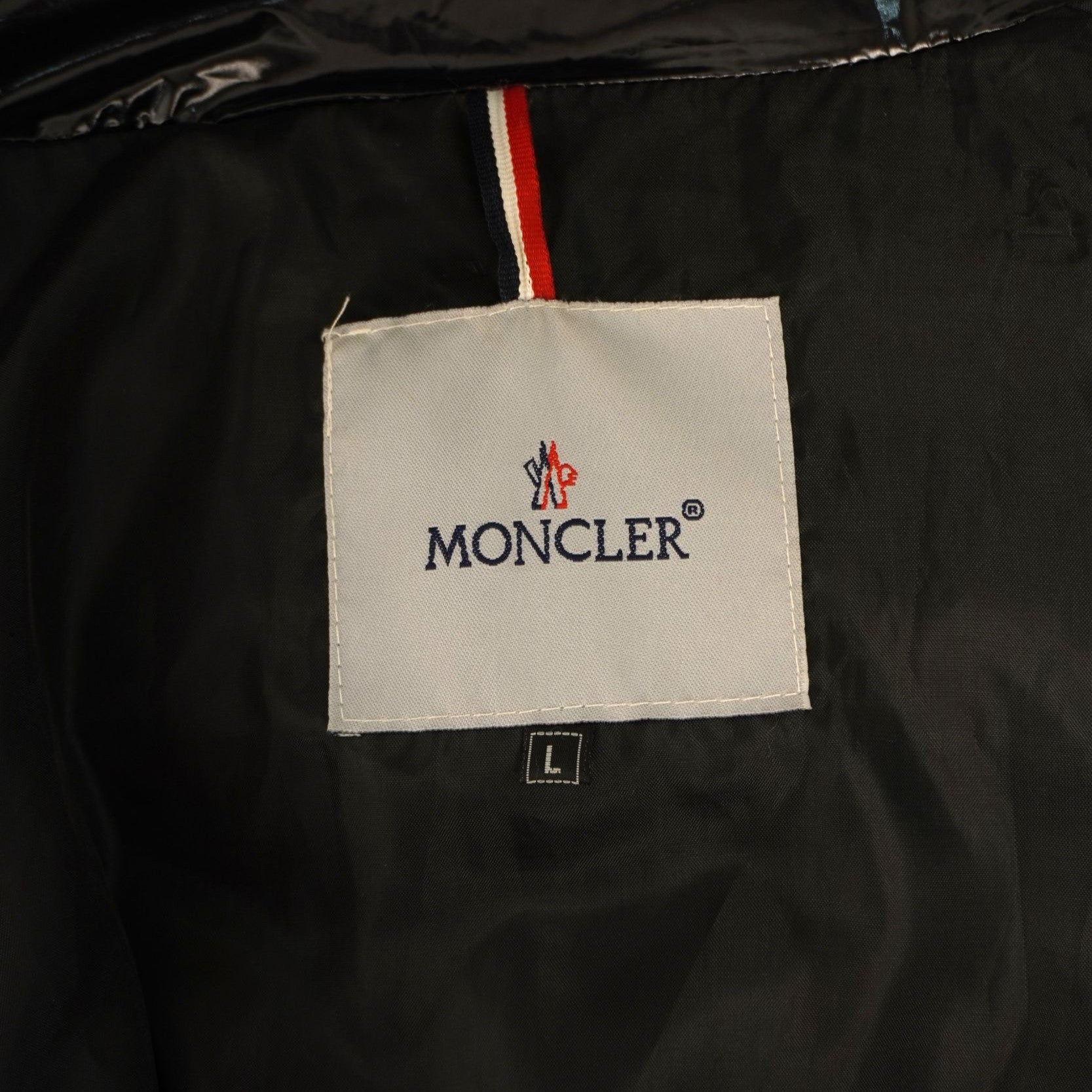 Primo piano dell'etichetta interna quadrata bianca con il logo ricamato Moncler e il passante con i colori della bandiera francese.
