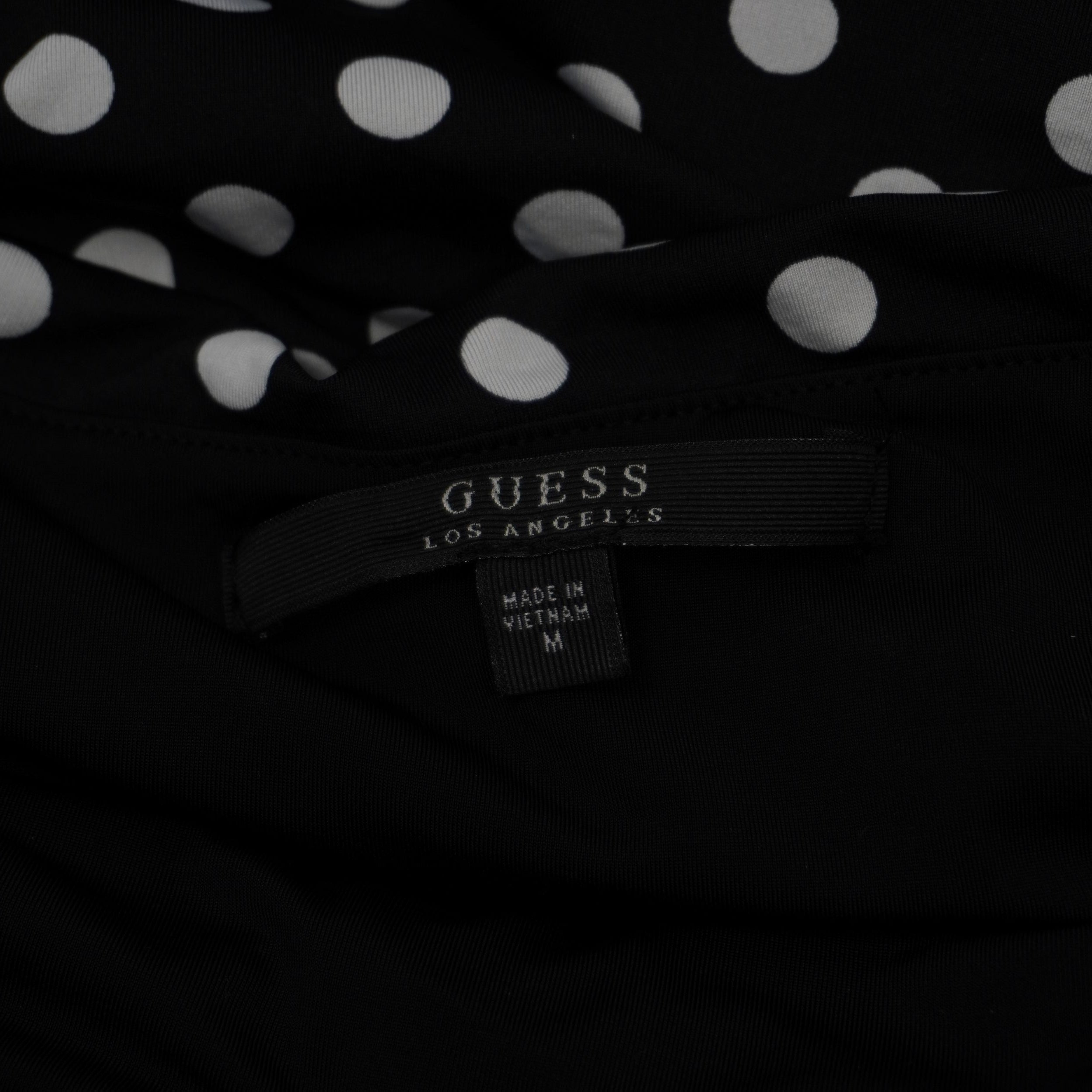 Etichetta interna in tessuto nero con logo GUESS Los Angeles e indicazione della taglia M cucita sul vestito.