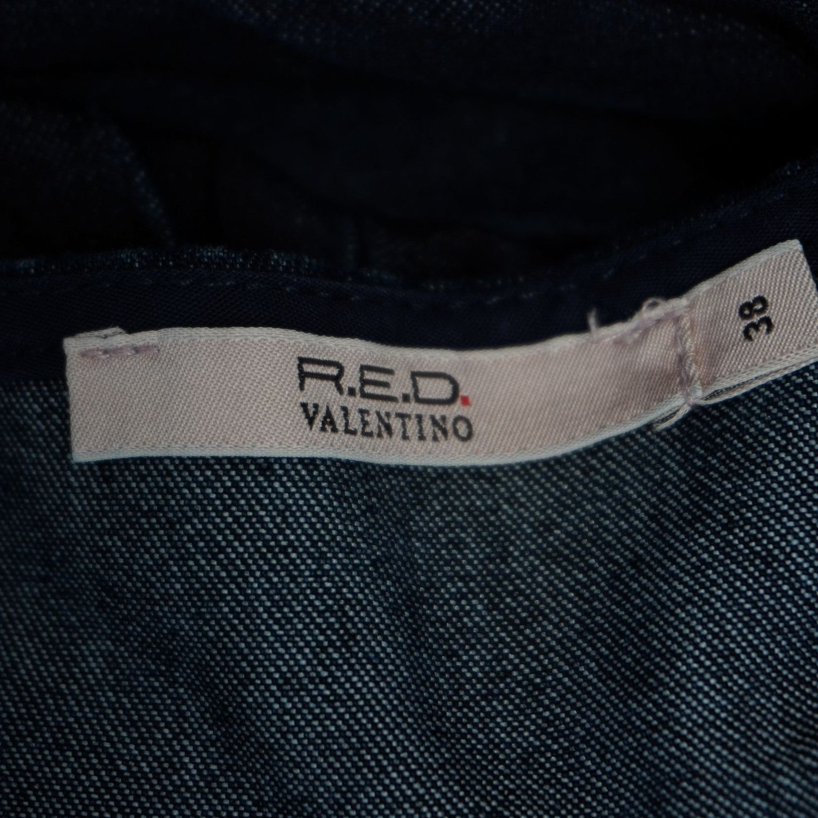Dettaglio dell'etichetta rettangolare chiara con il logo R.E.D. Valentino cucita all'interno della scollatura.