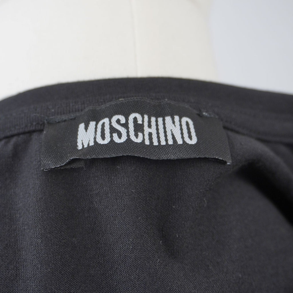 Dettaglio dell'etichetta in tessuto nero con la scritta bianca Moschino cucita internamente sul retro del colletto.