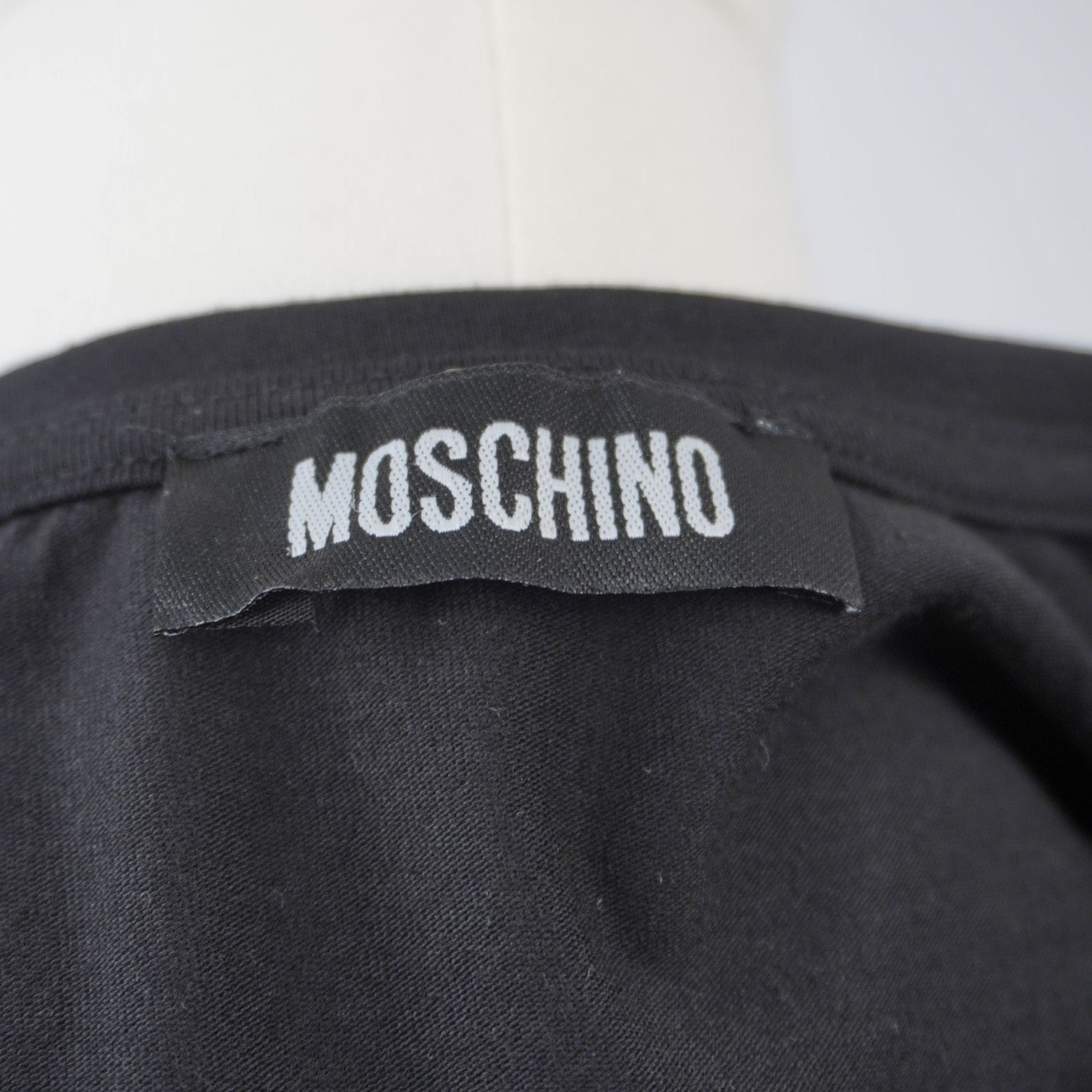 Dettaglio dell'etichetta in tessuto nero con la scritta bianca Moschino cucita internamente sul retro del colletto.