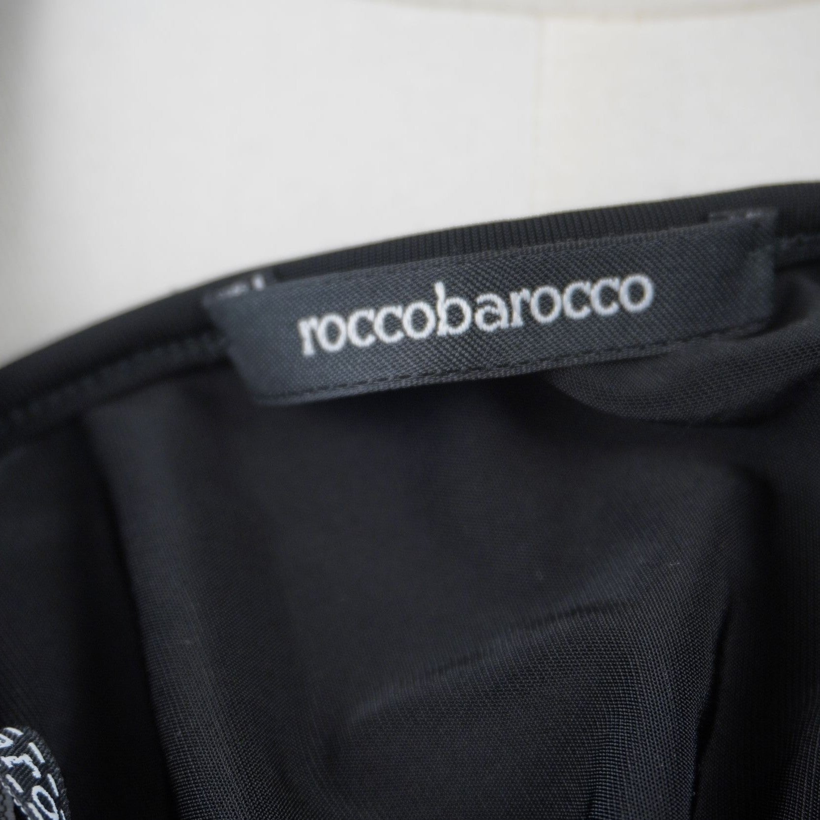 Dettaglio dell'etichetta rettangolare nera con il marchio Roccobarocco cucita sulla finitura interna del bordo.
