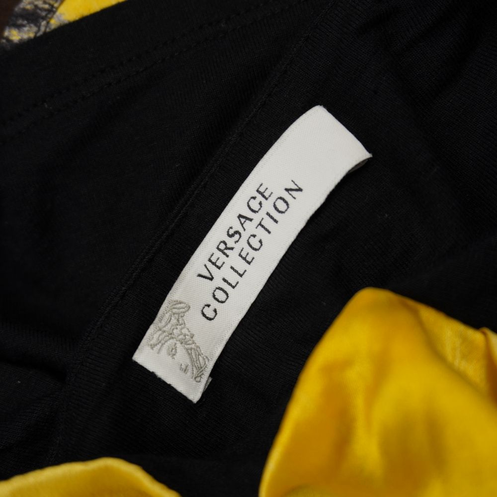 Etichetta interna in tessuto bianco con scritte nere che certifica il marchio Versace Collection, posizionata vicino al bordo del tessuto in seta gialla.
