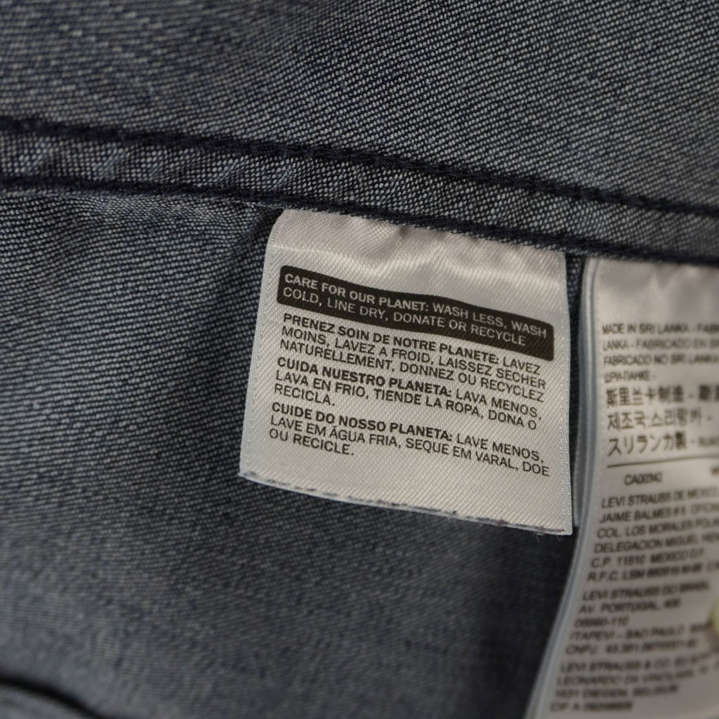 Inquadratura del tag interno bianco che riporta i codici identificativi di produzione della camicia di jeans.