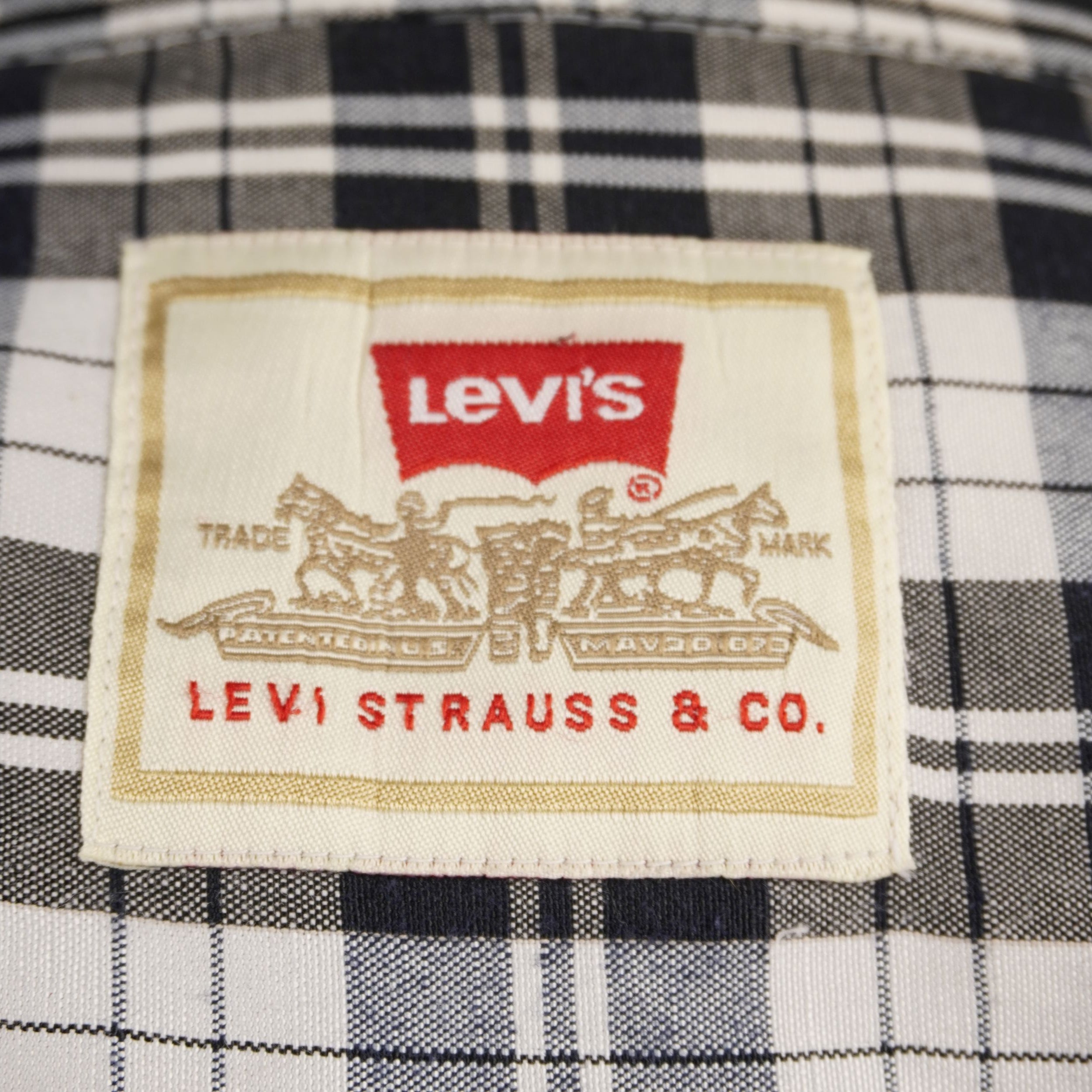  Primo piano dell'etichetta ricamata Levi Strauss & Co con logo a pipistrello rossa e bianca cucita sul colletto interno di una camicia a quadri.