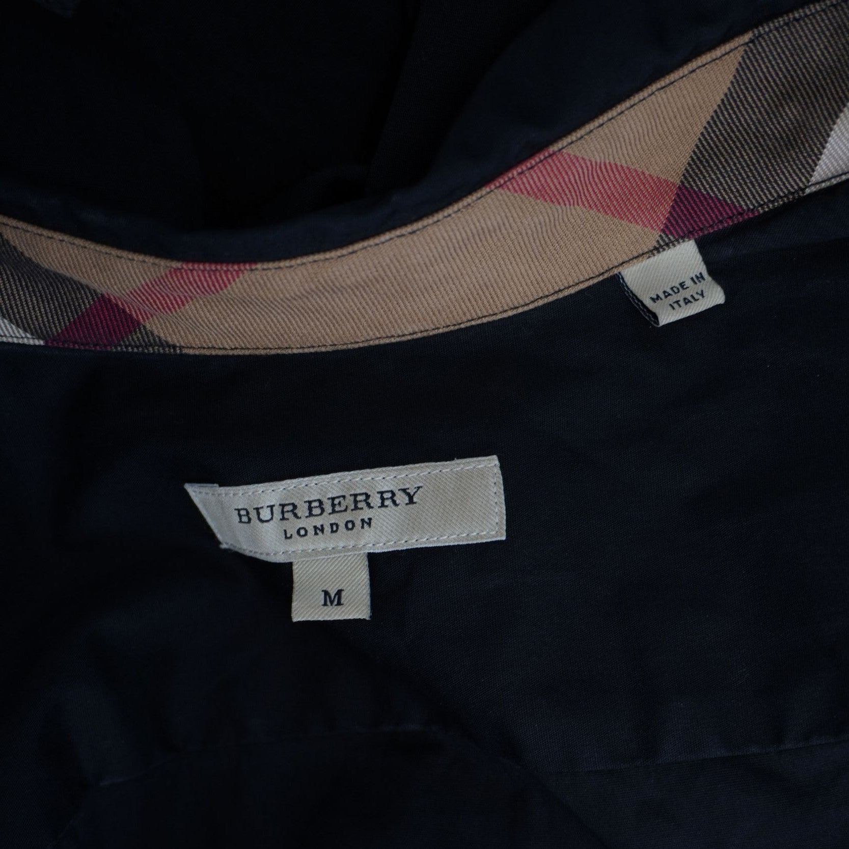 Primo piano della label bianca rettangolare Burberry London cucita sul retro del collo con l'indicazione della taglia M.